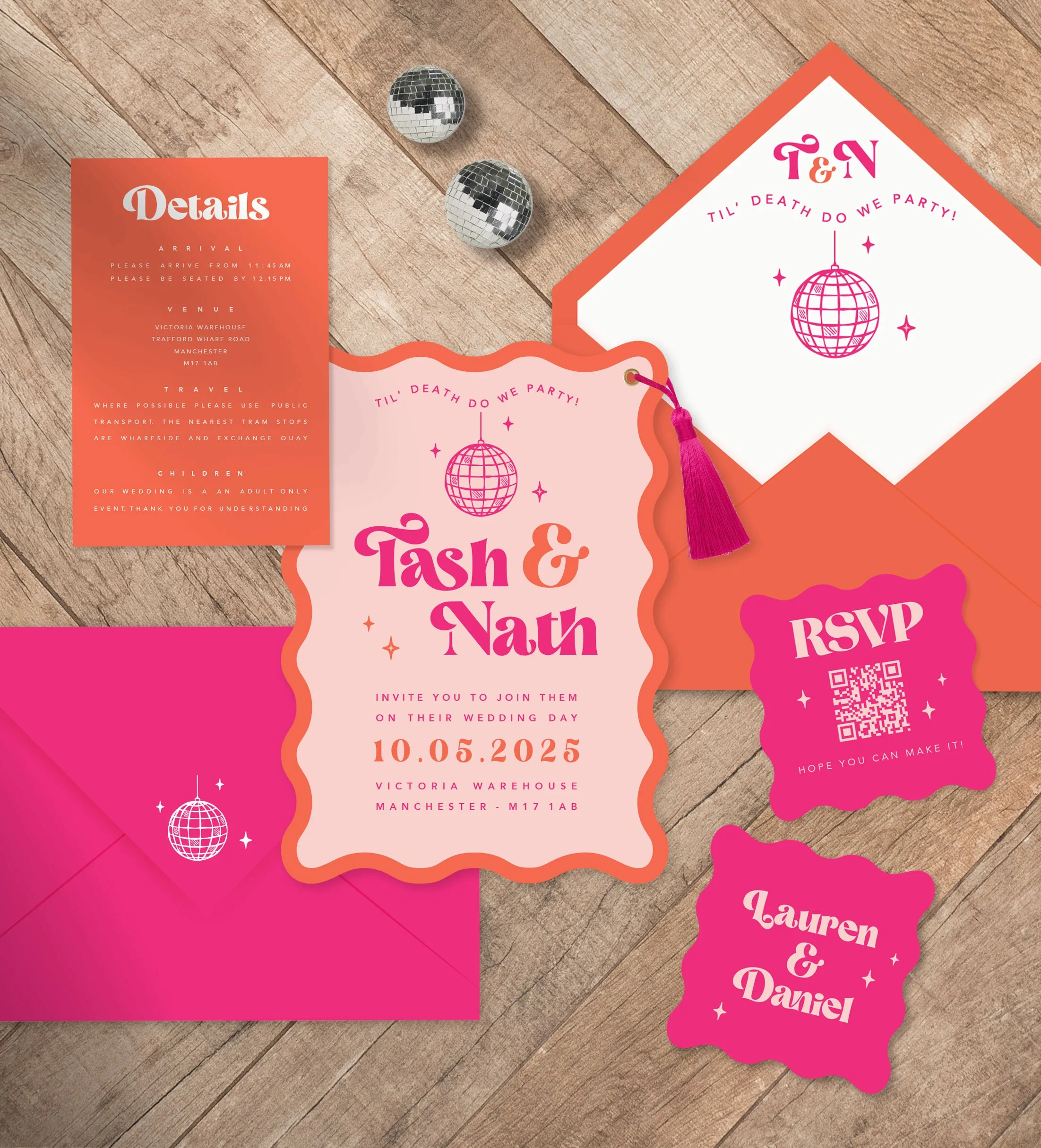 A wedding invitation set with pink and orange themed cards, RSVP, and details, on a wooden surface with two disco balls in the background.