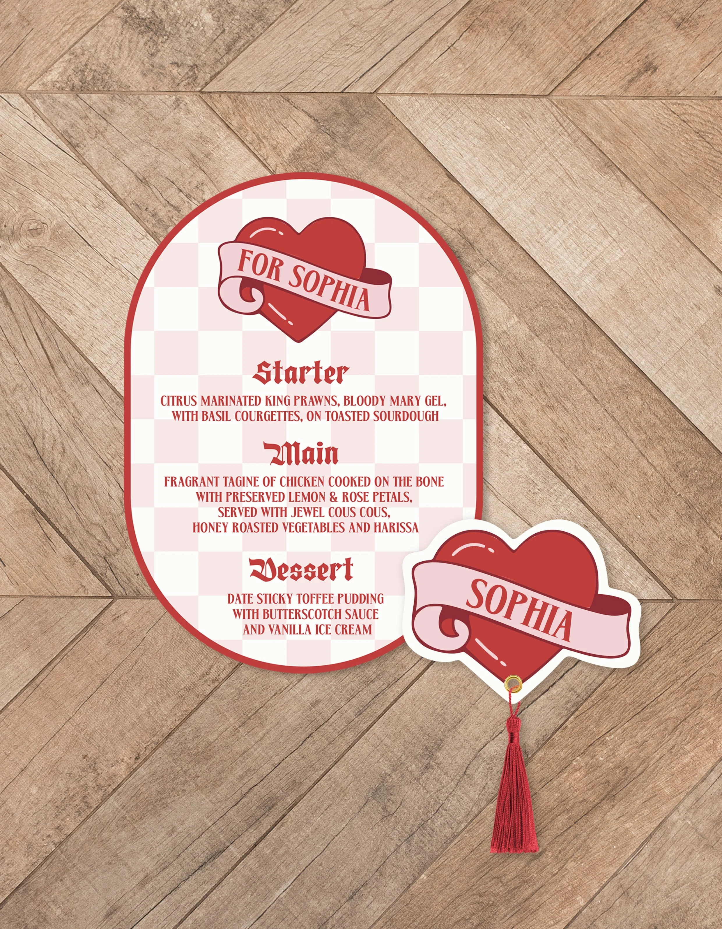 Valentine-themed restaurant menu titled 'For Sophia,' featuring a heart-shaped graphic with a banner and a name tag with a tassel. The menu lists a starter of citrus marinated king prawns, main course of fried chicken with lemon and rose petals, and dessert of date sticky toffee pudding with butterscotch sauce and vanilla ice cream, set on a wooden floor.