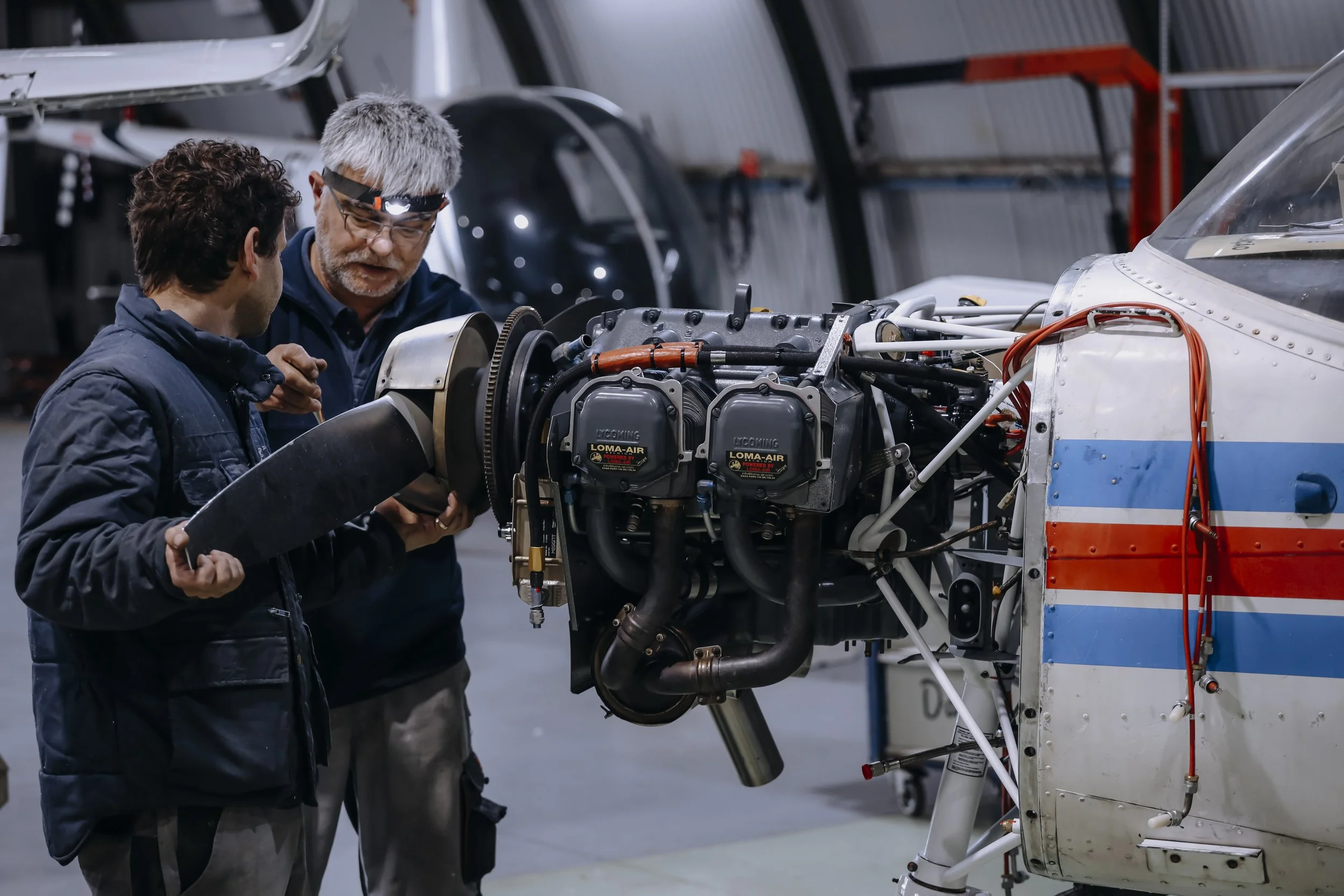 Dois homens trabalhando no motor de uma aeronave em uma oficina de aviões.