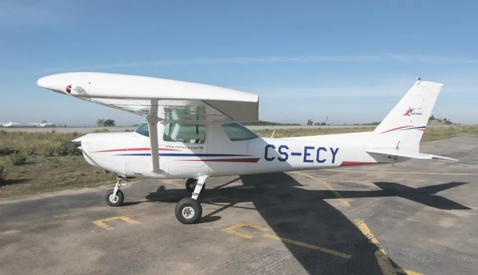 Avião pequeno com asa alta e trem de pouso fixo, estacionado na pista de aeroporto ao ar livre em dia ensolarado.