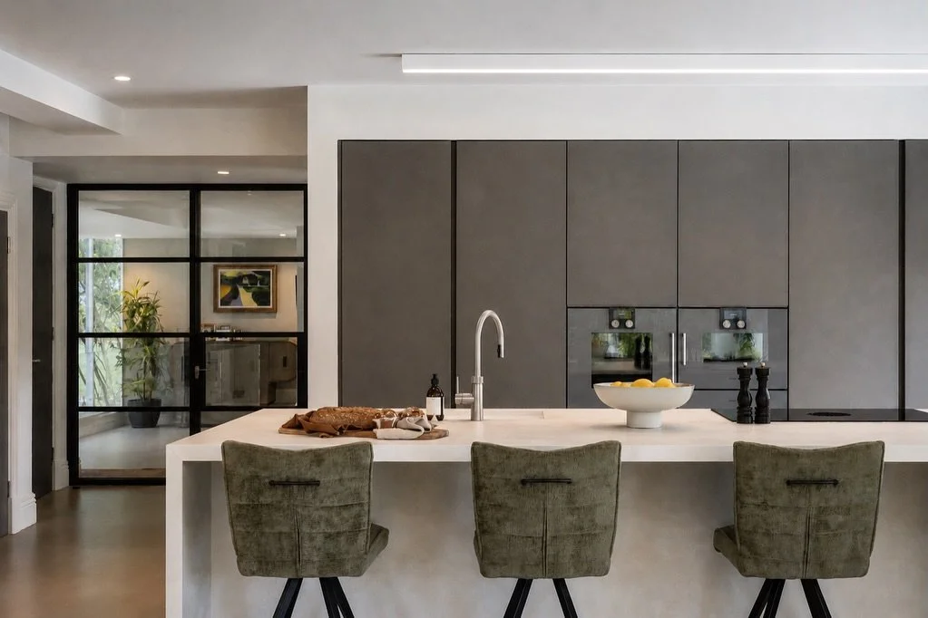 A contemporary kitchen we designed around a softer palette of concrete, mixed stone surfaces and a microcement media wall. With the island being such a dominant feature within the space, we wanted to break up its mass by introducing a sculptural butc