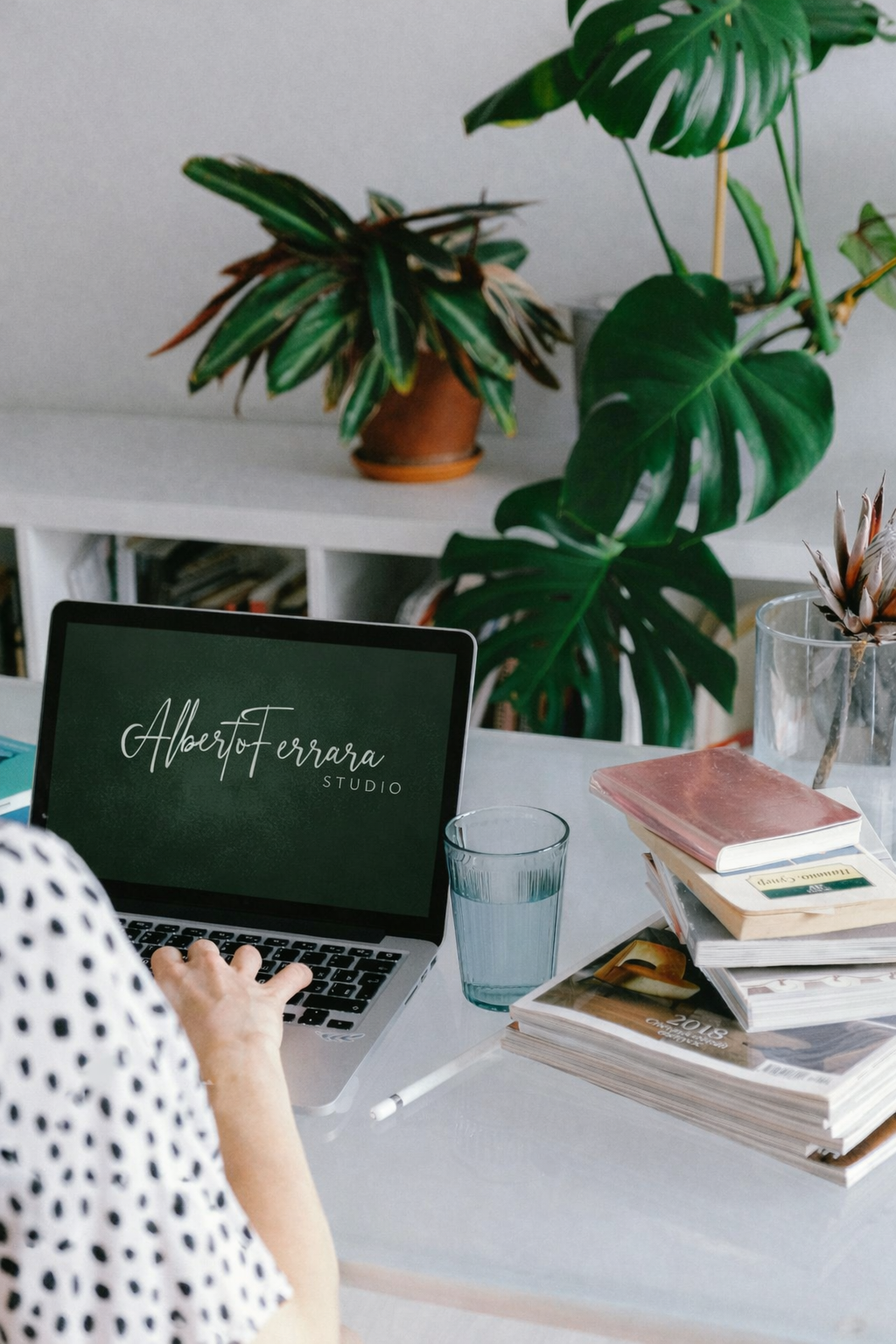 Un computer portatile con la scritta 'Alberto Ferrara Studio' sullo schermo, accanto a tazze, libri e piante verdi in un ambiente di lavoro.