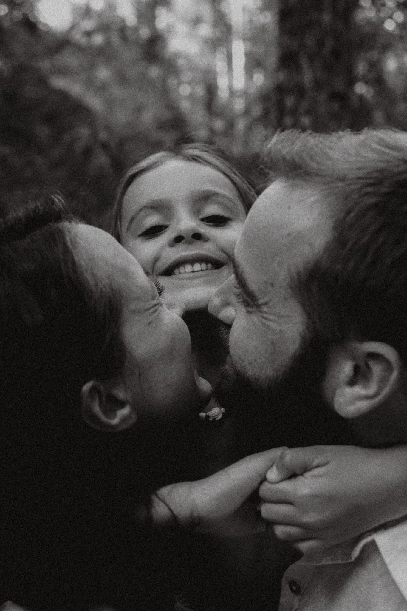Una familia comparte un abrazo en un entorno natural, con la niña sonriendo en el centro mientras sus padres la rodean con cariño.