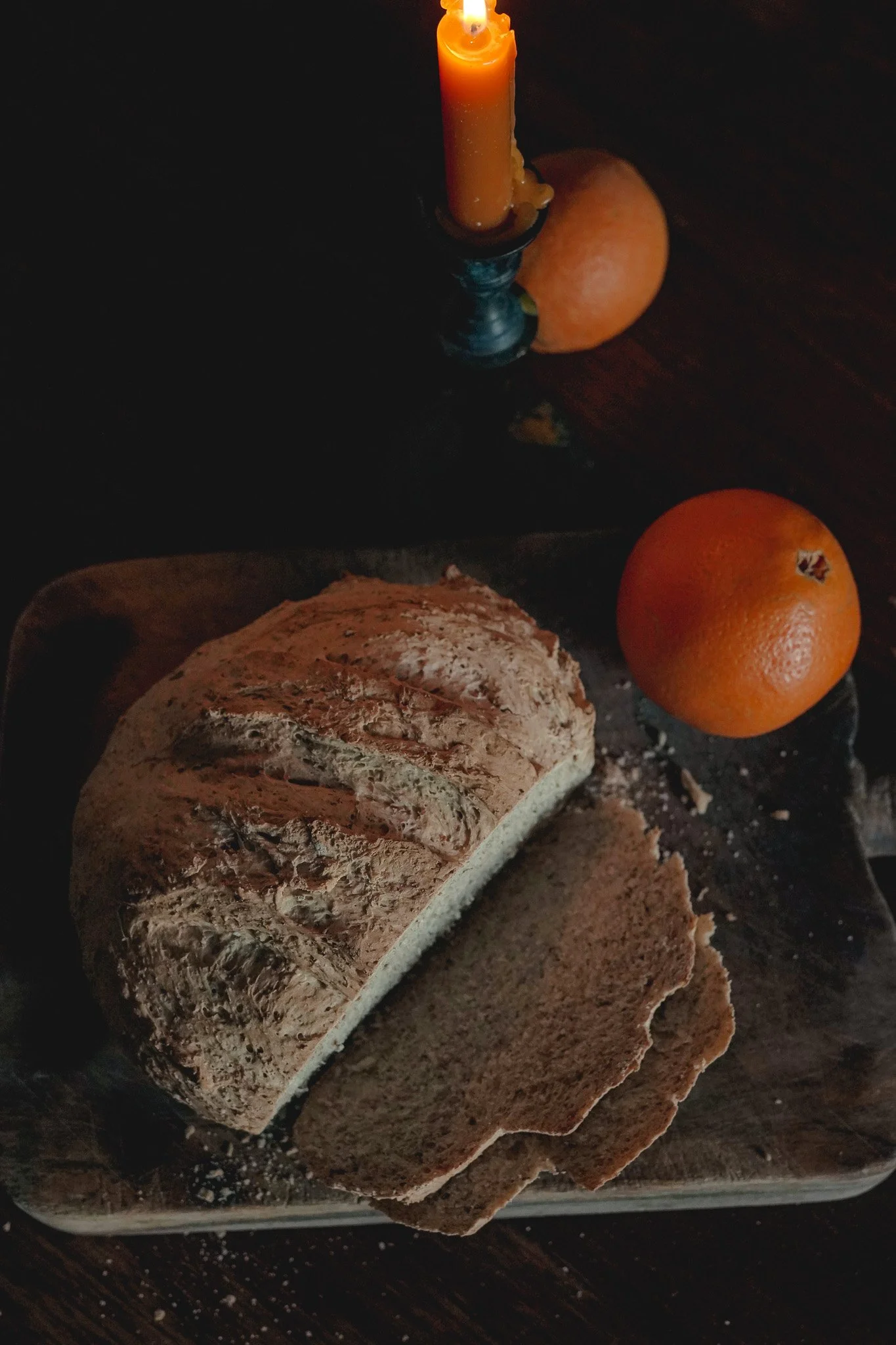 Pan de caja sobre un plato, dos naranjas y una vela encendida en un fondo oscuro.