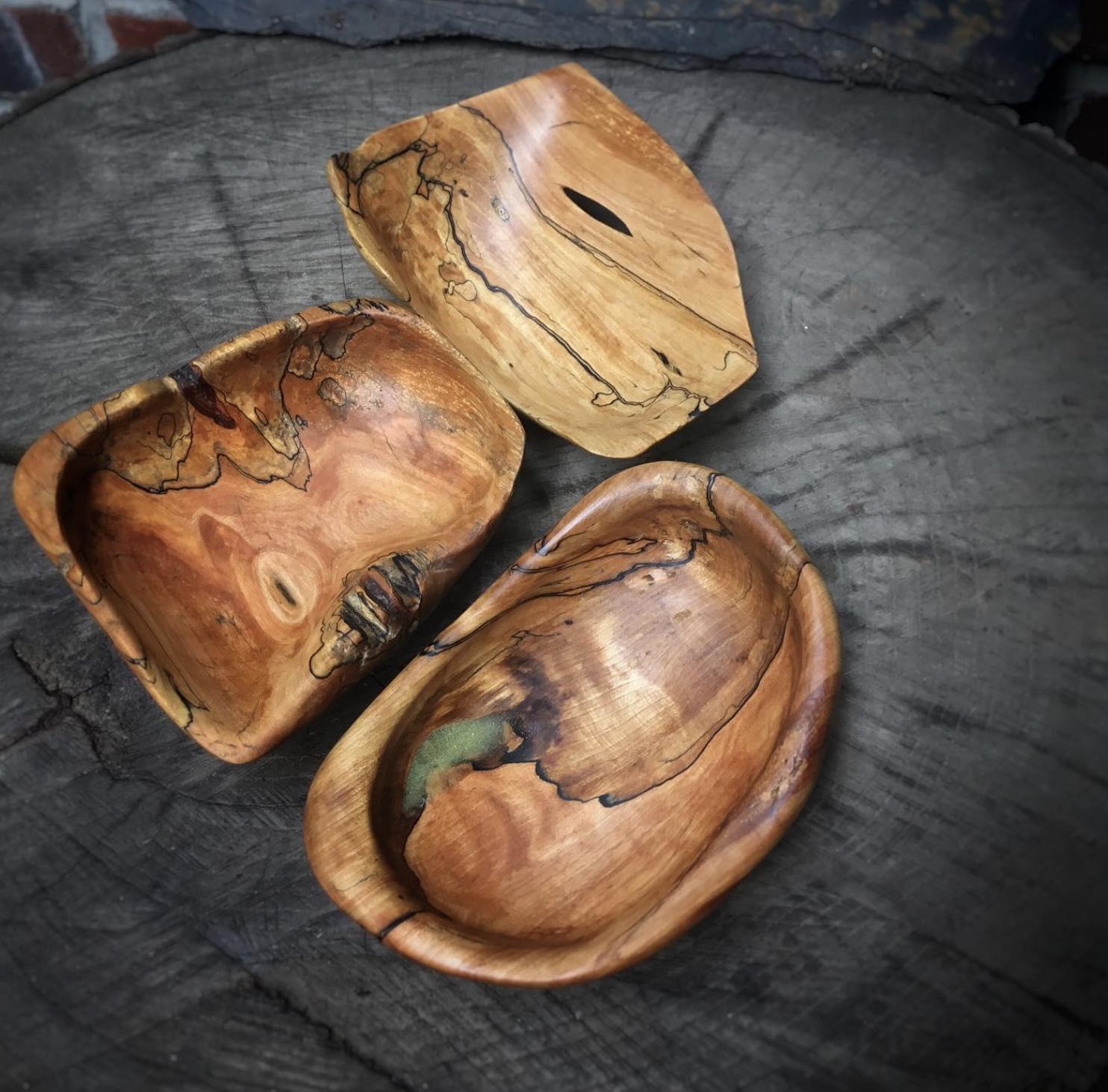 Trois petits bols en bois de différentes formes, posés sur une surface en bois foncé.