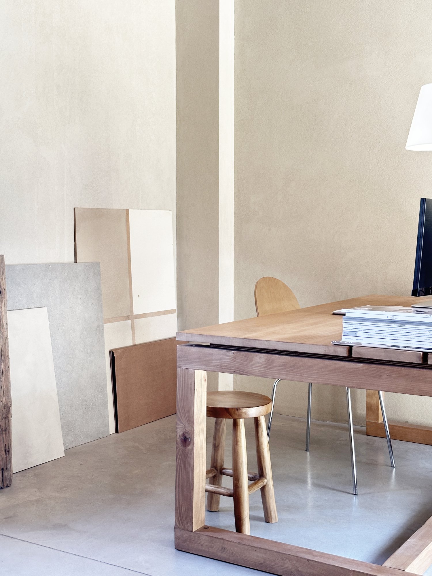 Interno di uno studio o ufficio con un Tavolo di legno, una sedia di legno e alcuni pannelli di materiali vari appoggiati contro il muro.