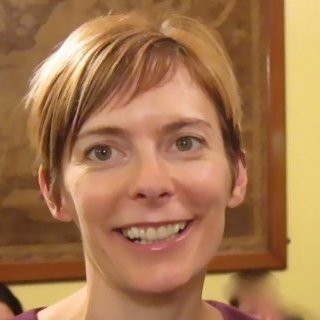 A smiling woman with short light brown hair in an indoor setting.
