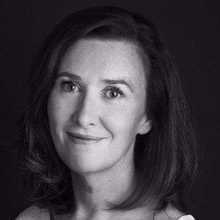 Black and white portrait of a woman with shoulder-length hair, smiling slightly, against a dark background.