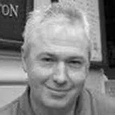 Black and white photo of a smiling man with short, light-colored hair.