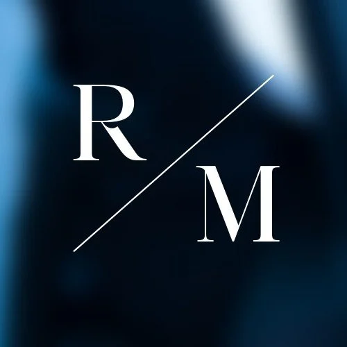 Stylized logo with the letters 'R' and 'M' separated by a diagonal line on a dark, blurred background.