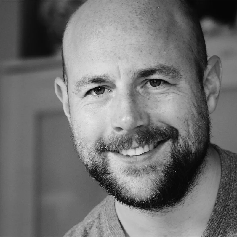 A smiling man with a beard and short hair in a close-up black-and-white portrait.