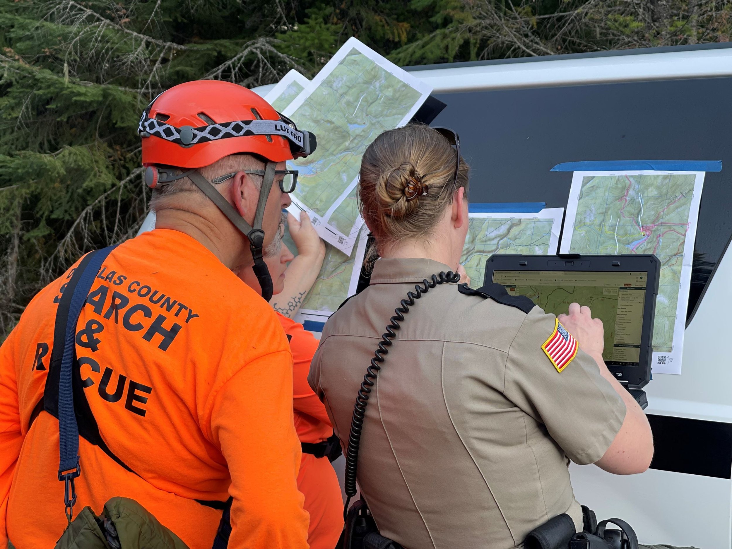 Search and rescue team members examining maps and a computer for finding a location in a wooded area.