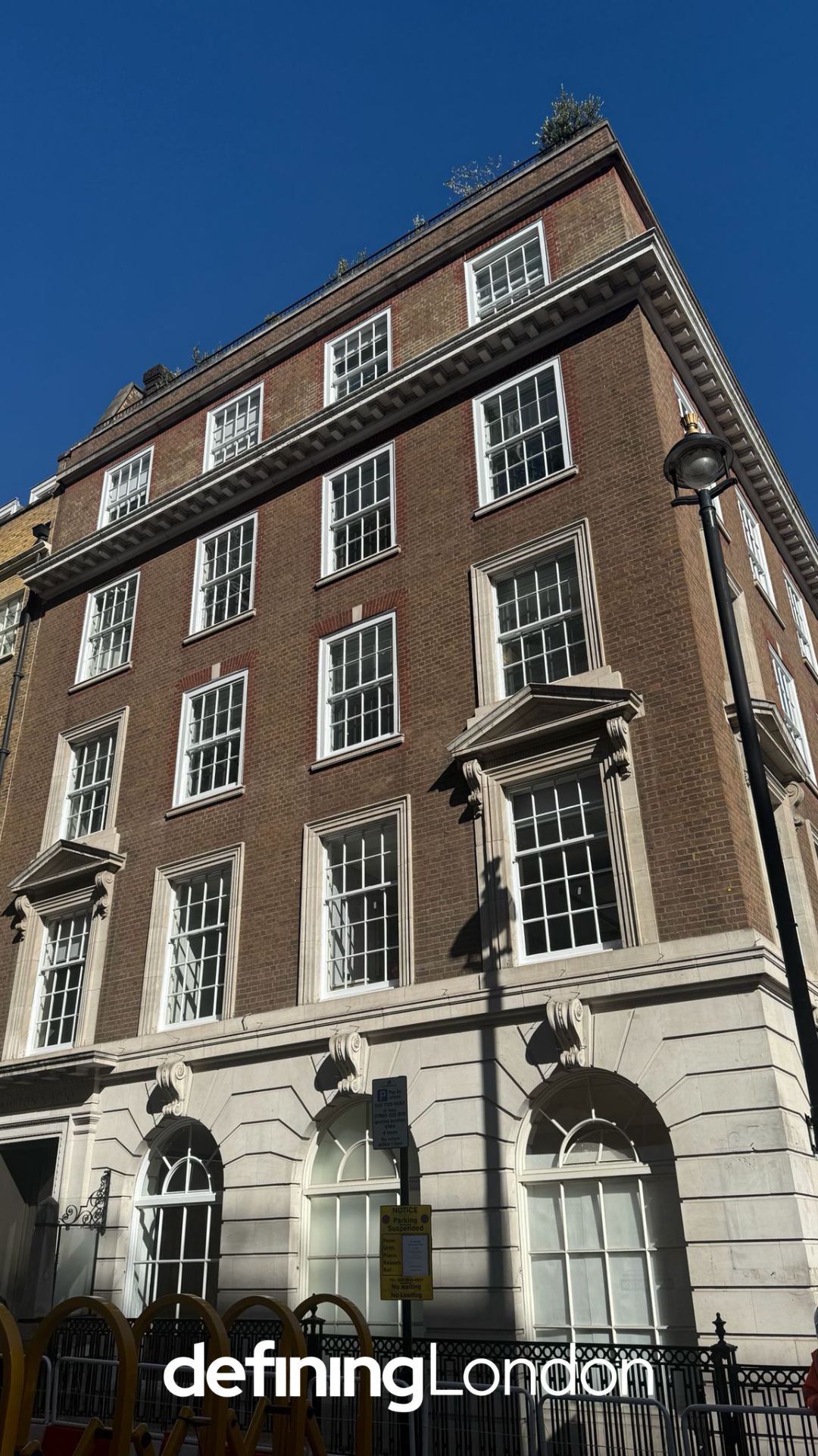 A tall multi-story brick building with white window frames and decorative architectural details, under a clear blue sky.