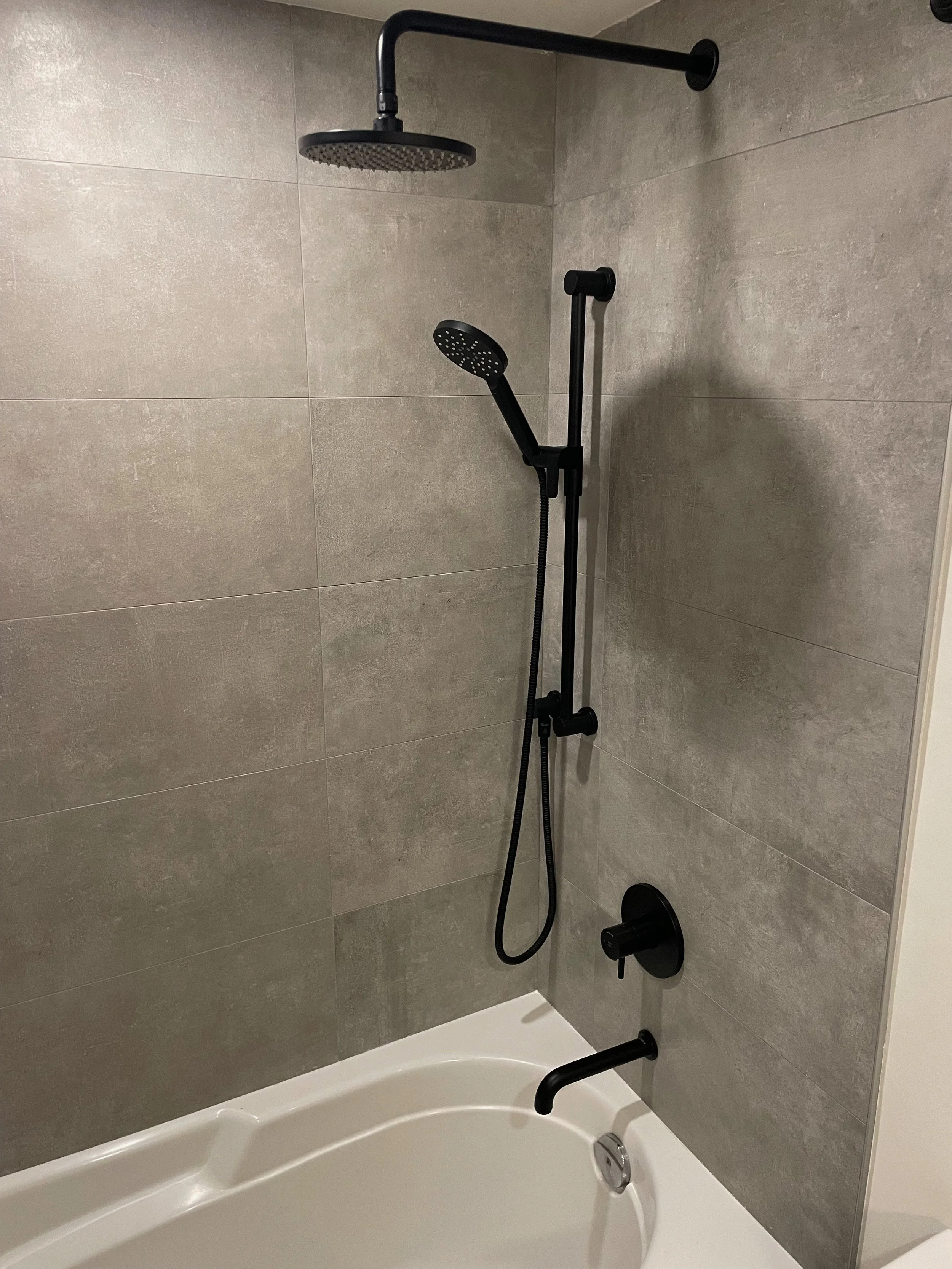 Modern shower with black fixtures, including a rain showerhead, a handheld shower, and a sliding bar, installed in a tiled bathroom.