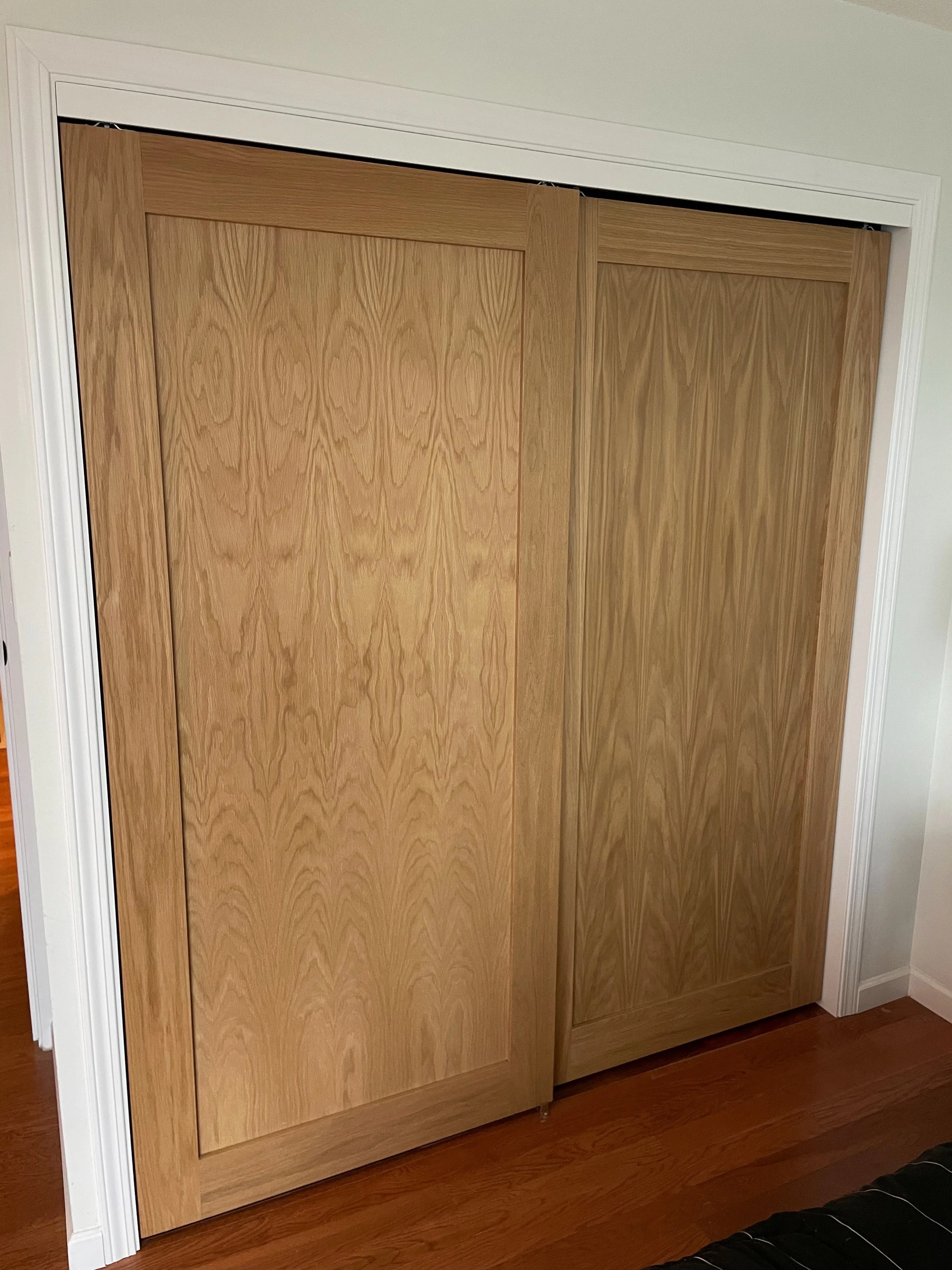 Wooden sliding closet doors in a room with white walls and hardwood flooring.