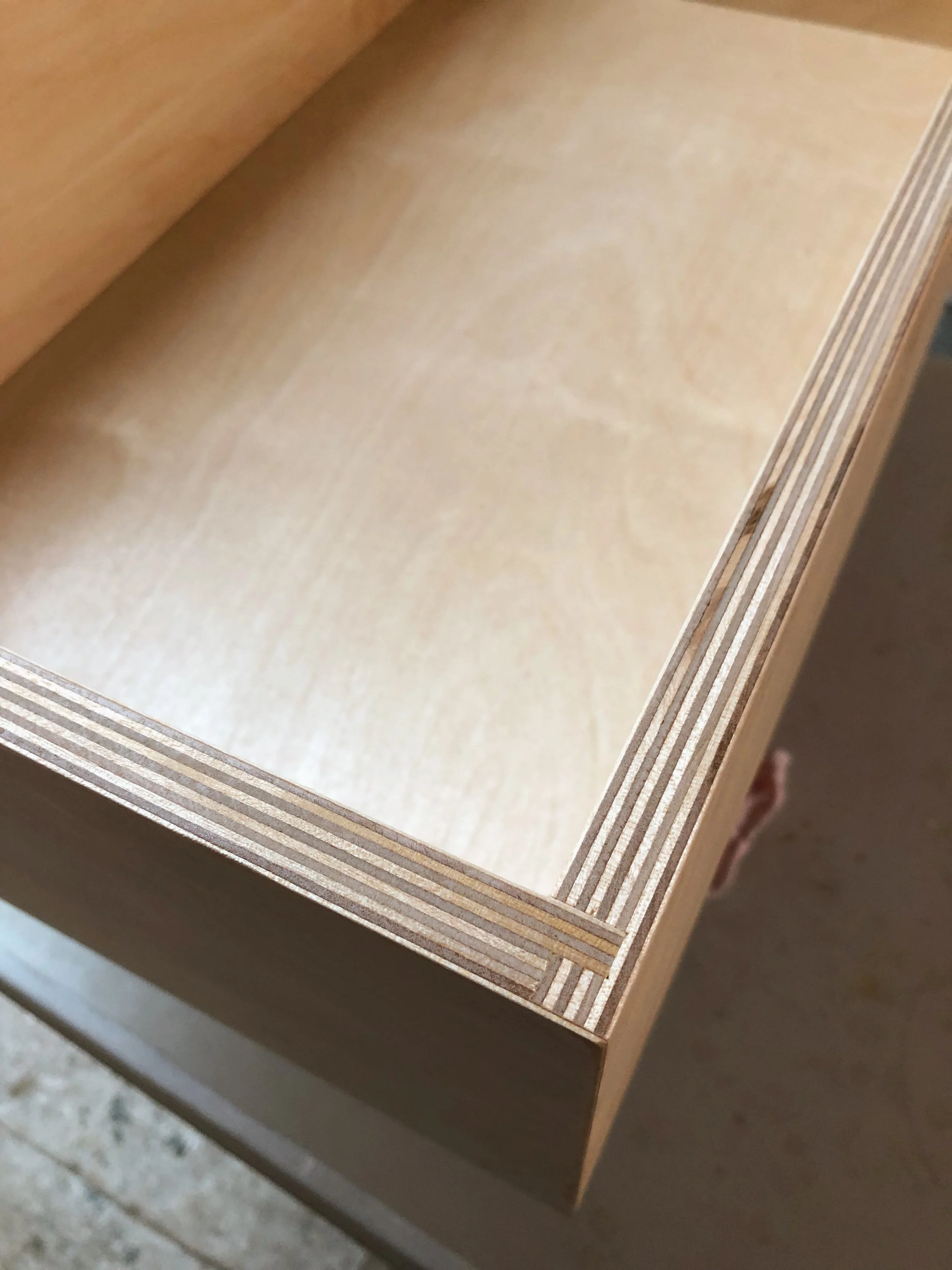Close-up of a wooden drawer with layered plywood edges, showing the interior and side view.