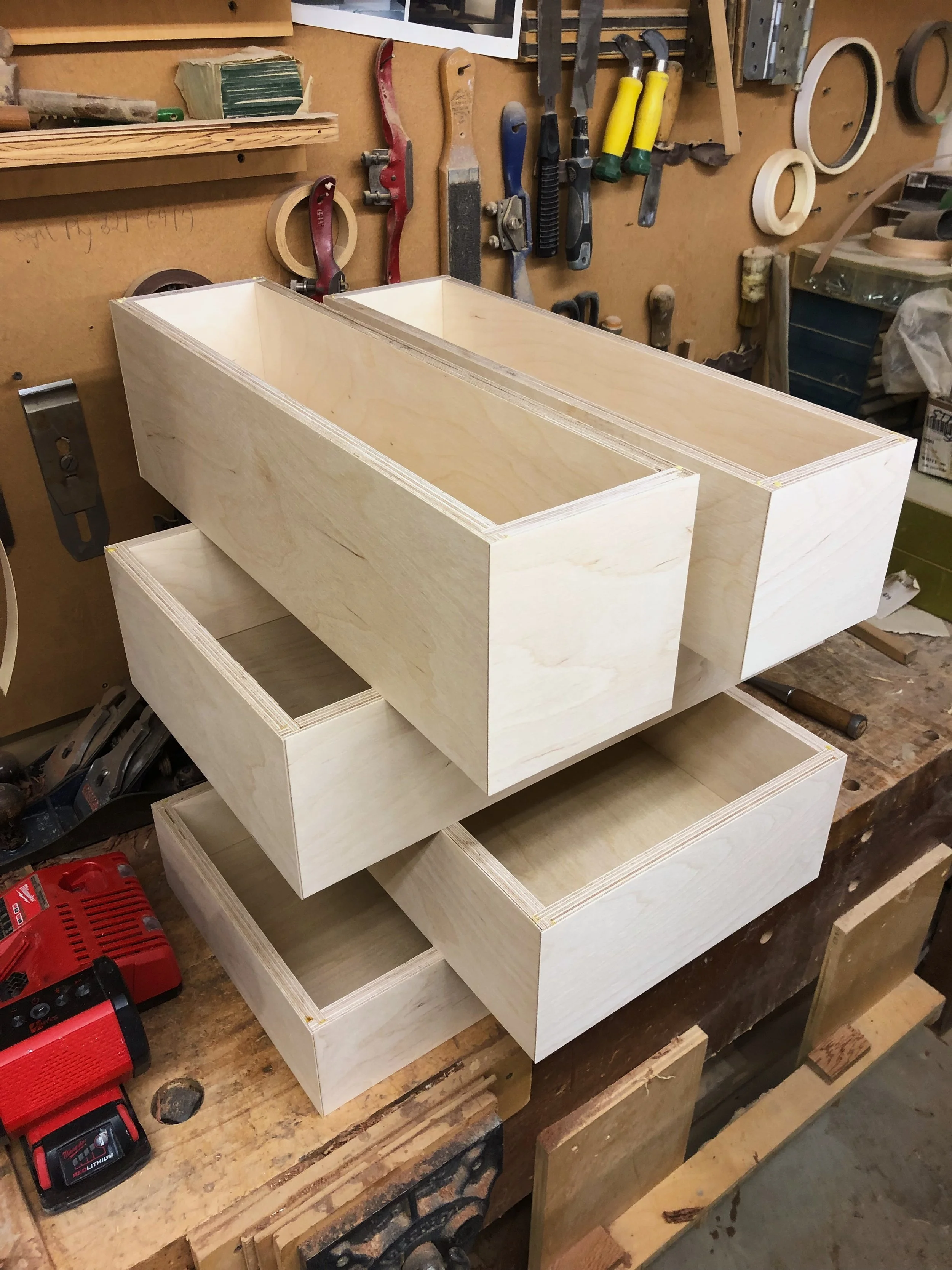 Stacked unfinished wooden boxes on a workbench in a woodworking shop.