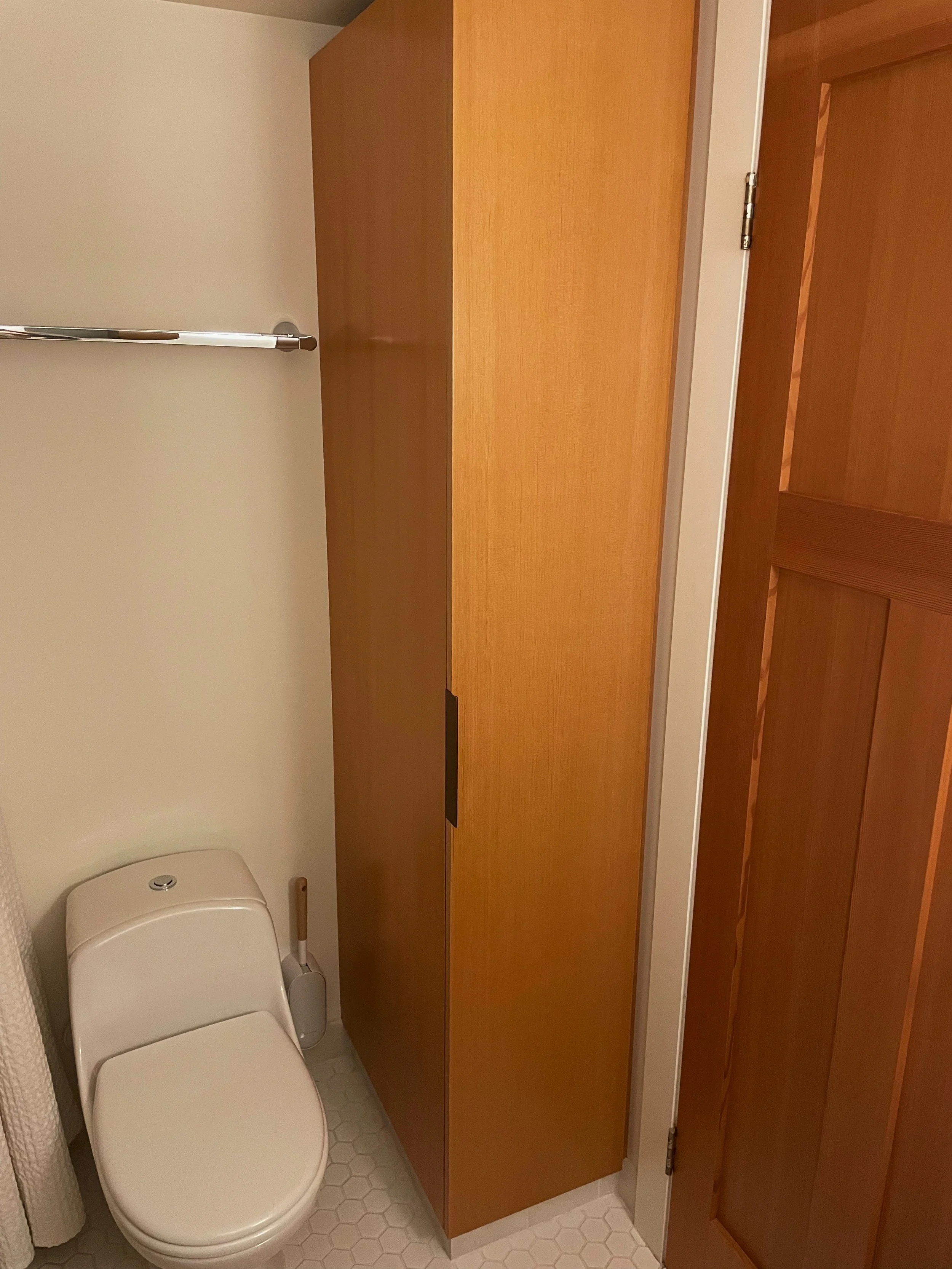 A small bathroom with a white toilet, a wooden cabinet, a shower curtain, hexagonal tiled floor, and a wooden door.