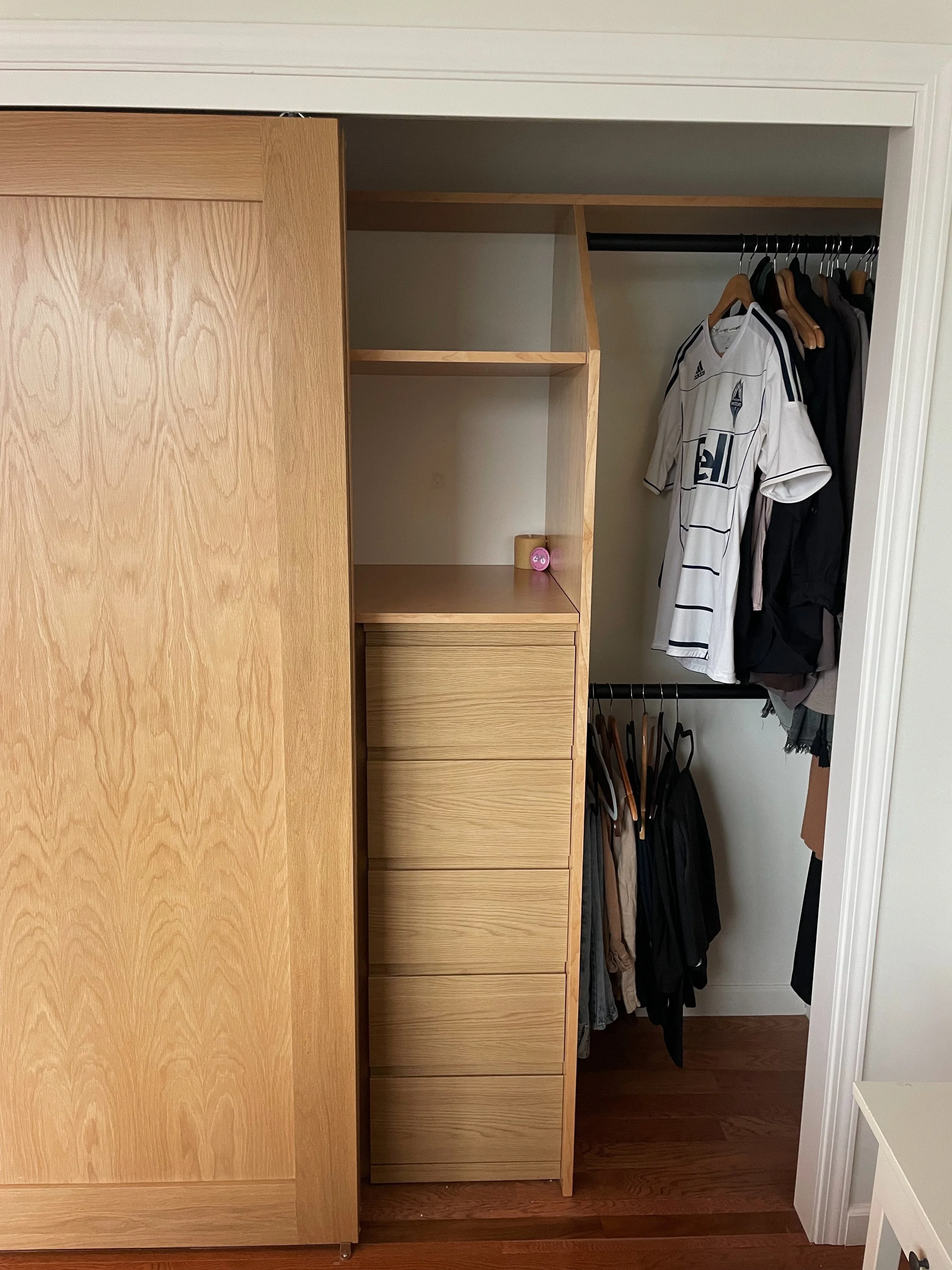 Interior of a closet with wooden shelves, drawers, and hanging space filled with clothes, including a white sports jersey and various jackets.