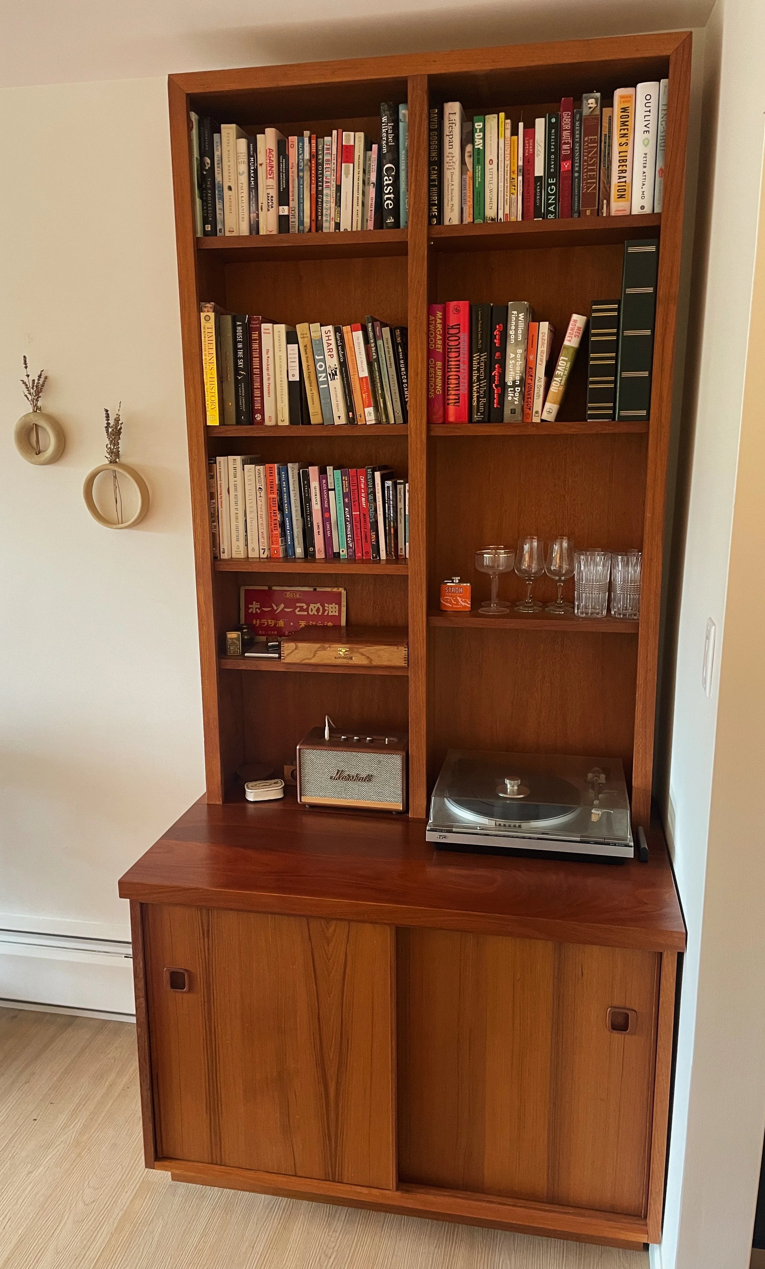 A wooden bookshelf with books, glasses, a Marshall speaker, and a record player on a wooden cabinet.