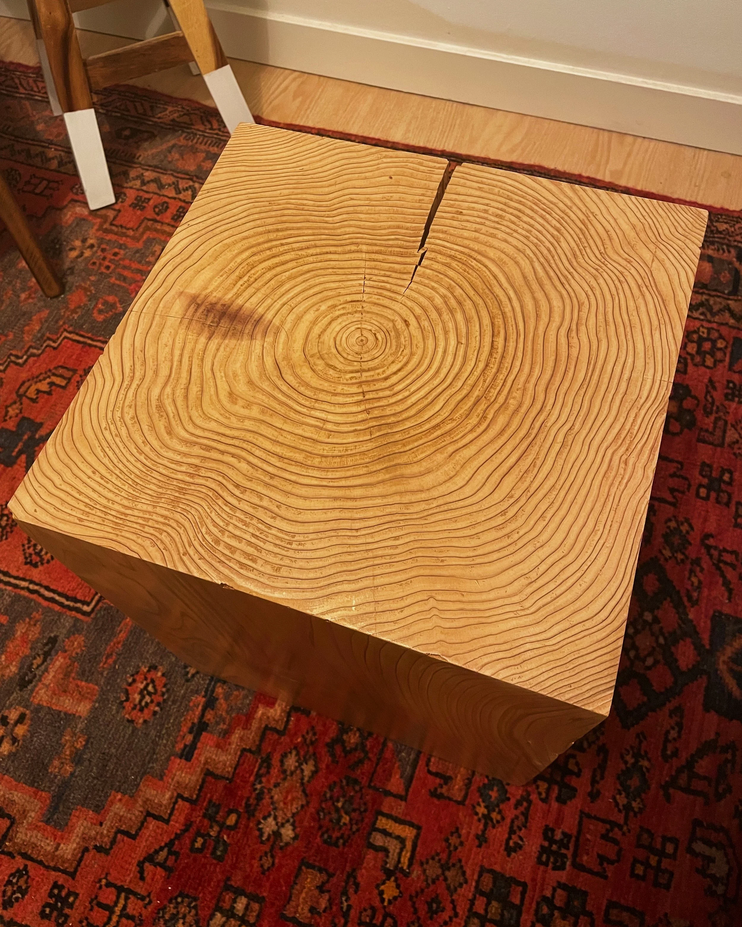A wooden cube table with a large crack in the top surface, showing concentric growth rings.