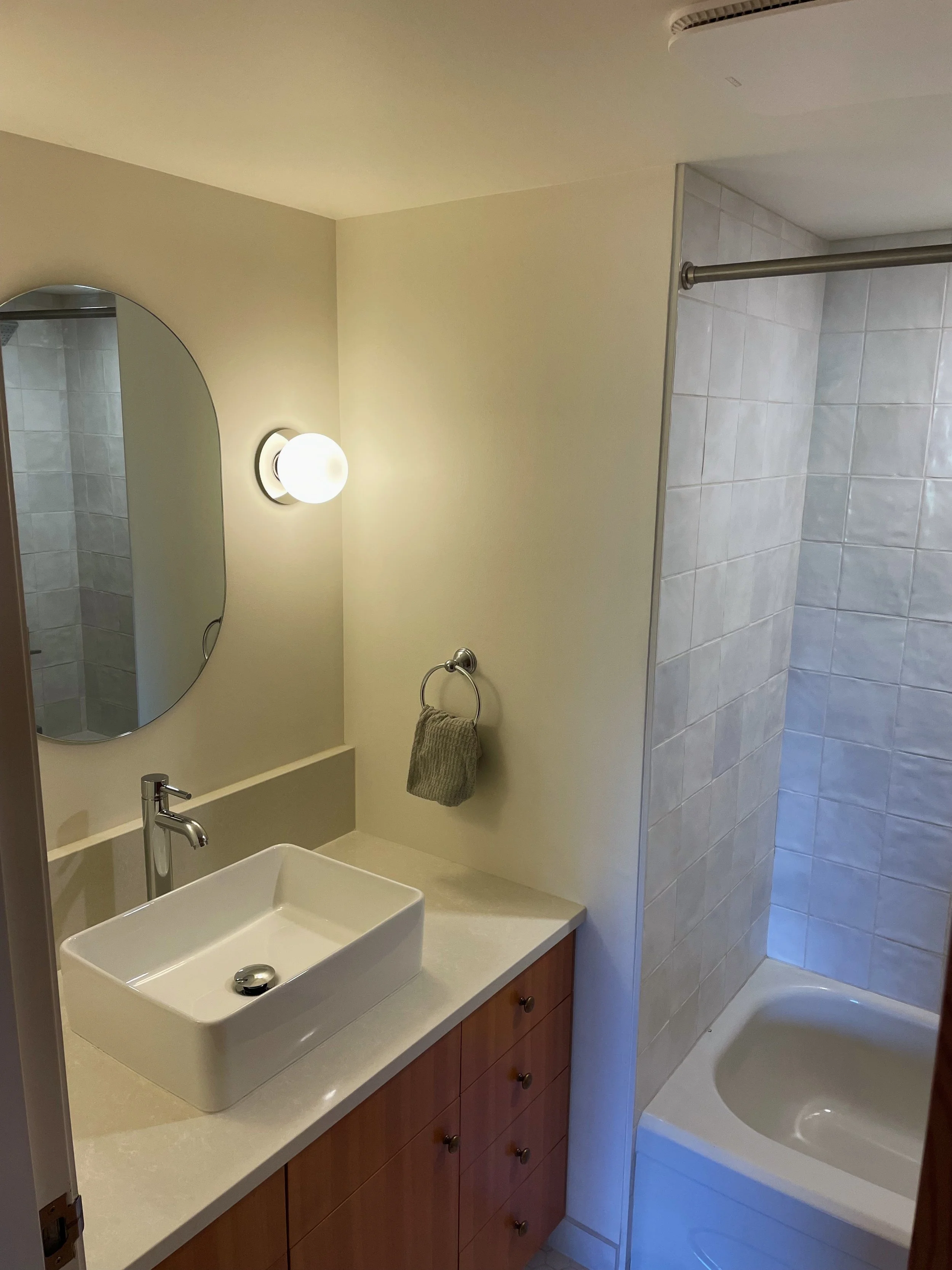 Bathroom with a vessel sink, mirror, wall sconce, towel ring with a gray towel, and a walk-in shower with a tiled wall.