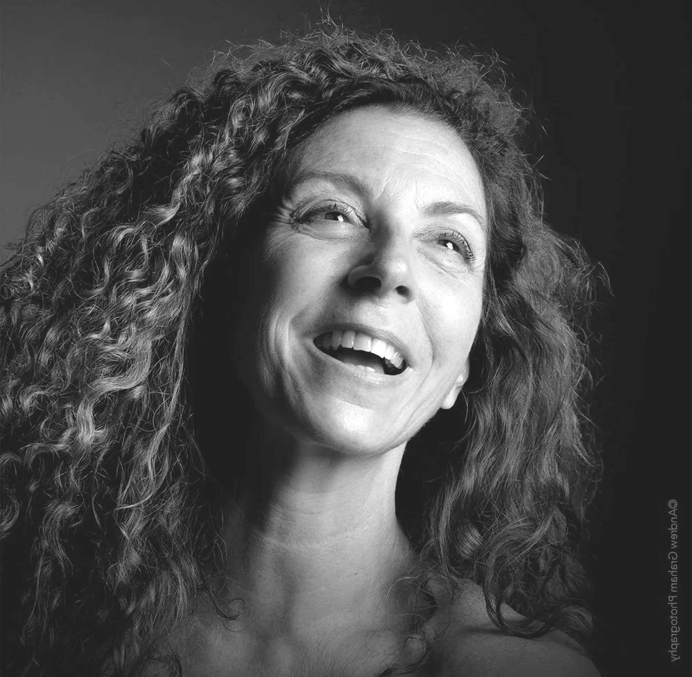 Black and white portrait of a woman with curly hair, smiling and looking upwards.