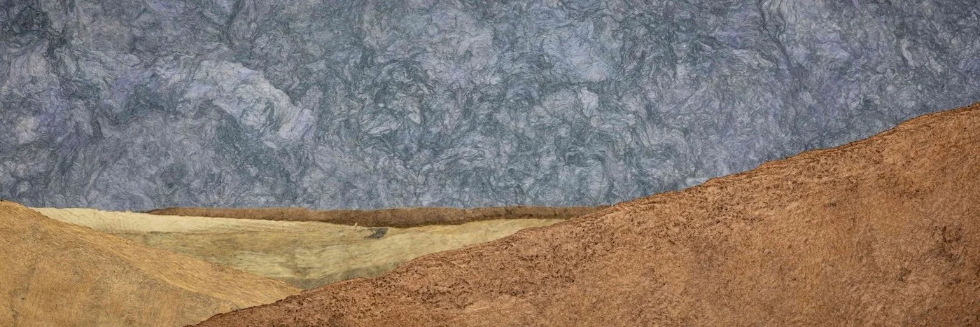 Mehrfarbige Schichten von Papier oder Stoff in Erdtönen und Blau, übereinandergelegt.