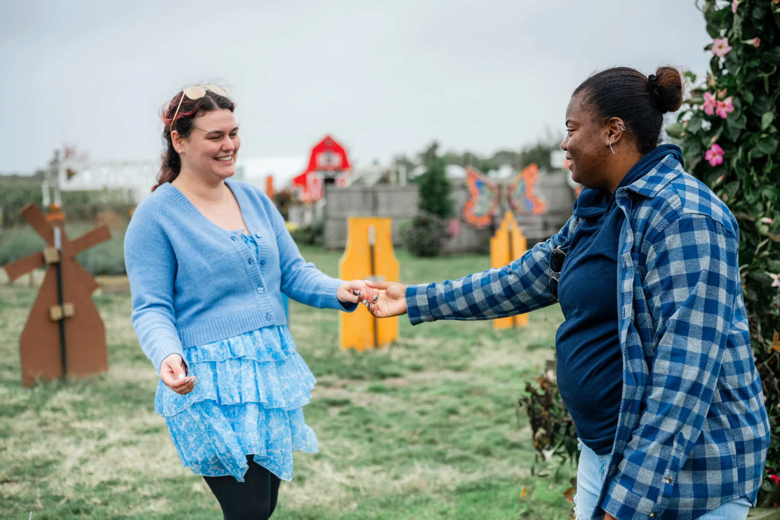 Two women holding hands and smiling outdoors near decorative butterfly and flower structures