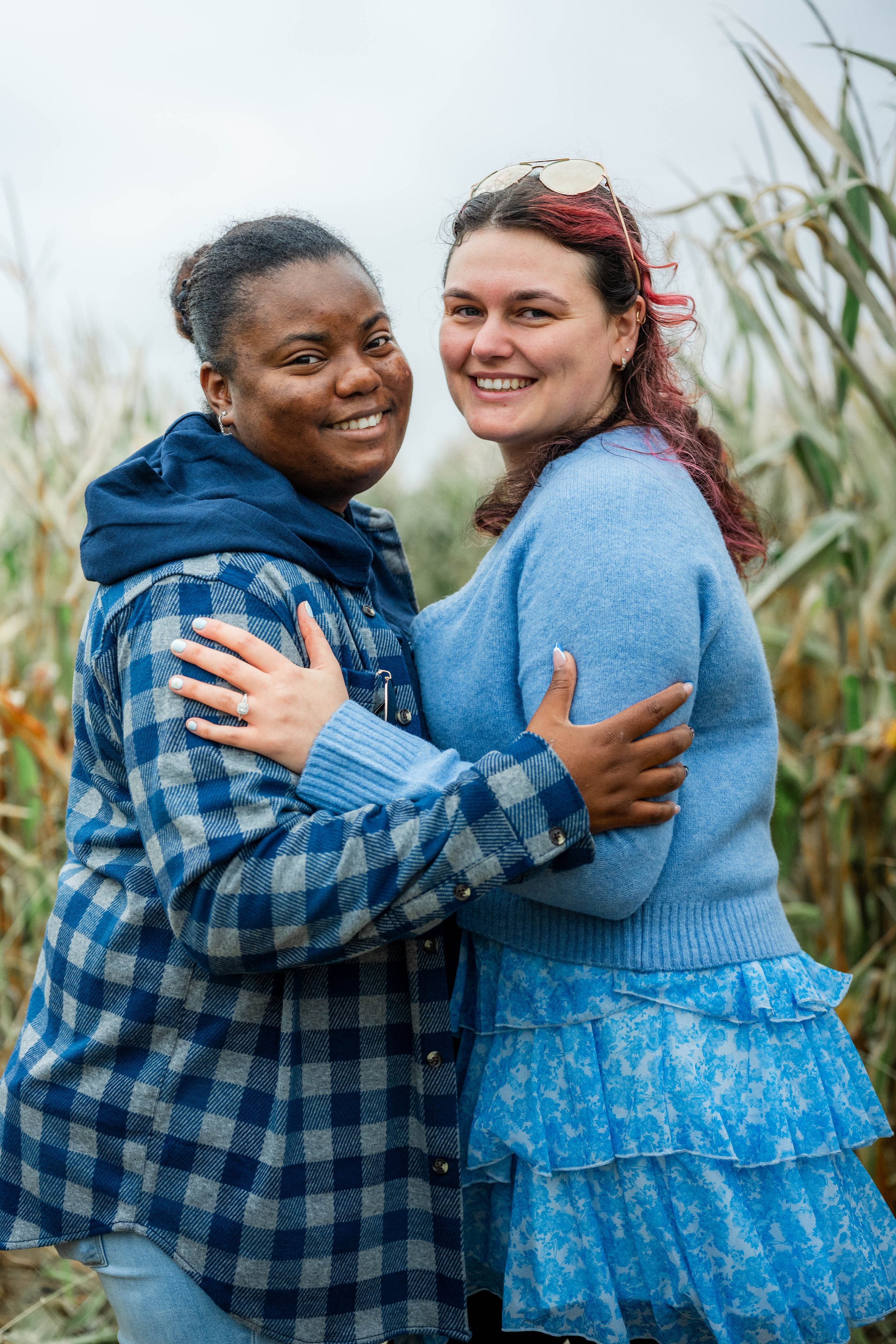 Two women standing close together in a cornfield, smiling and hugging each other.