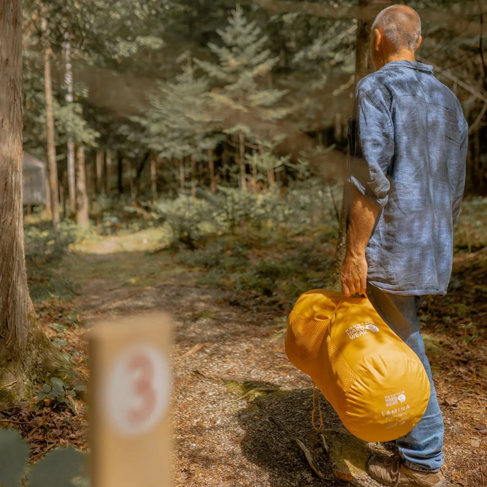 Homme marchant en forêt avec un sac de couchage, dans un contexte d’immersion en nature