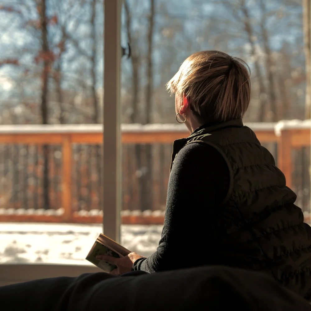 Personne devant une fenêtre de l'éco-chalet Ontara donnant sur un paysage hivernal, suggérant l'introspection et la contemplation.