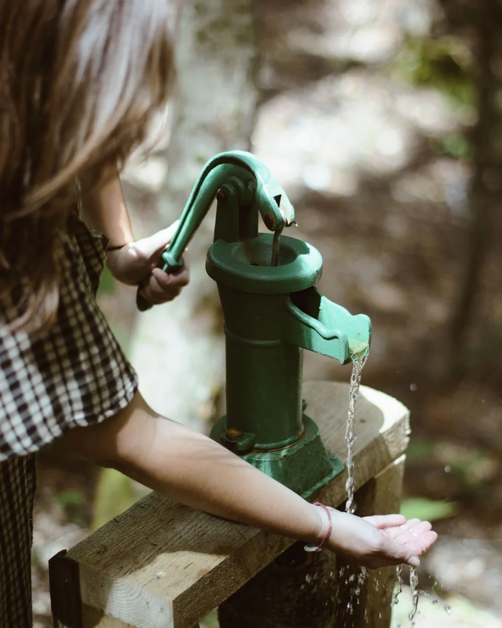Femme pompant l'eau pure d'une source, illustrant la gestion écoresponsable de l'eau sur le site.