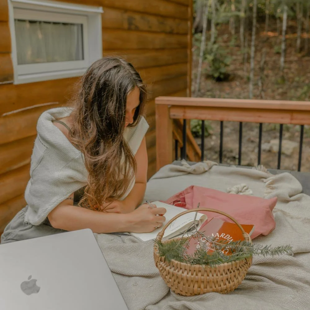 Femme sur un patio d'un chalet en forêt écrivant dans un cahier