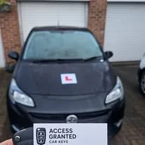 Black car with learner driver sign on the hood, parked in front of garages.