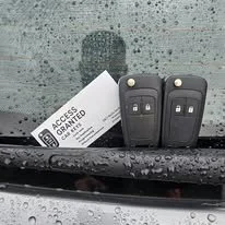 Two car keys with key fobs and a VIP access card on a wet car windshield