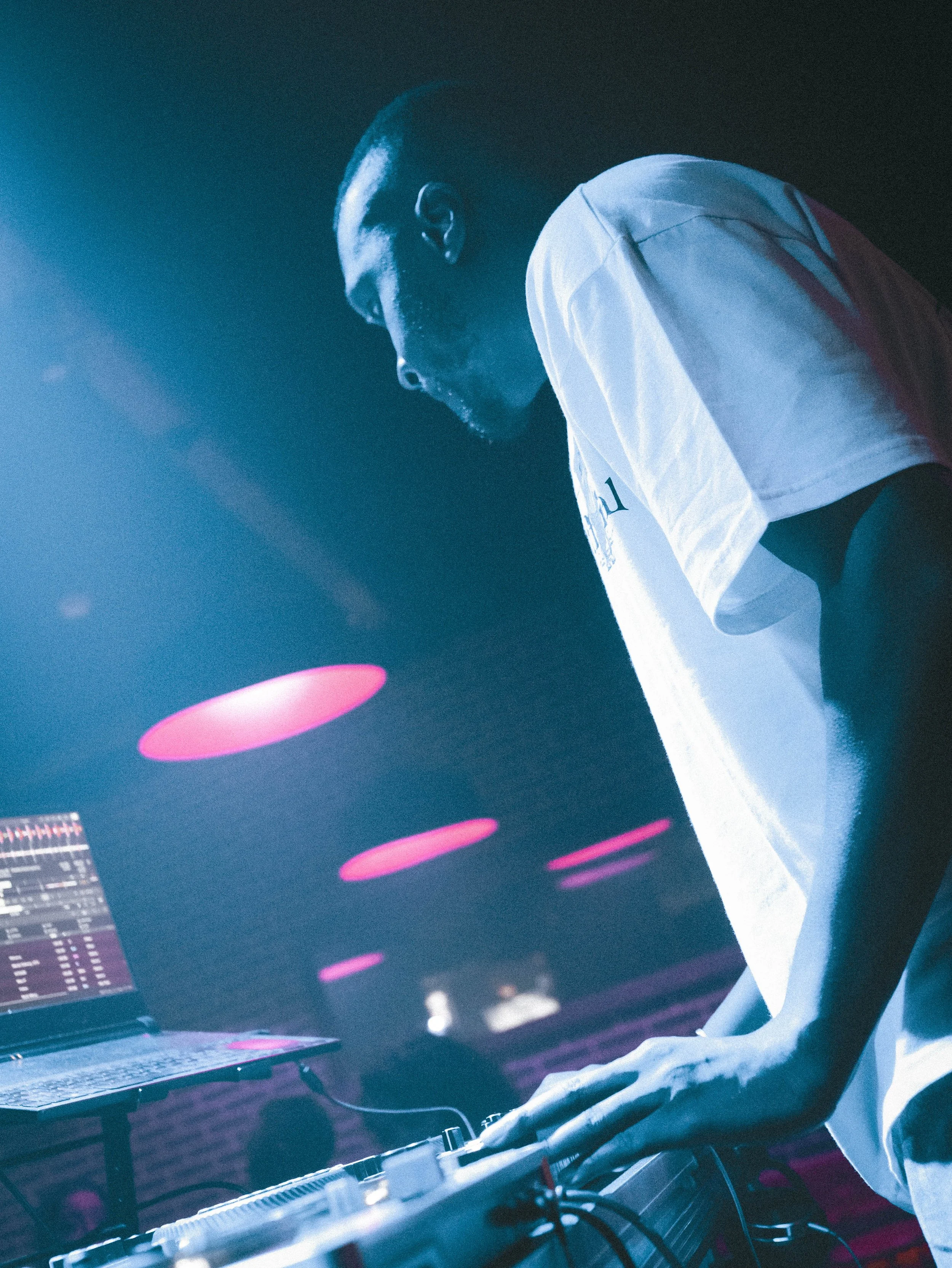DJ ou musicien utilisant un équipement de mixage dans une ambiance sombre avec des lumières violettes ou roses.