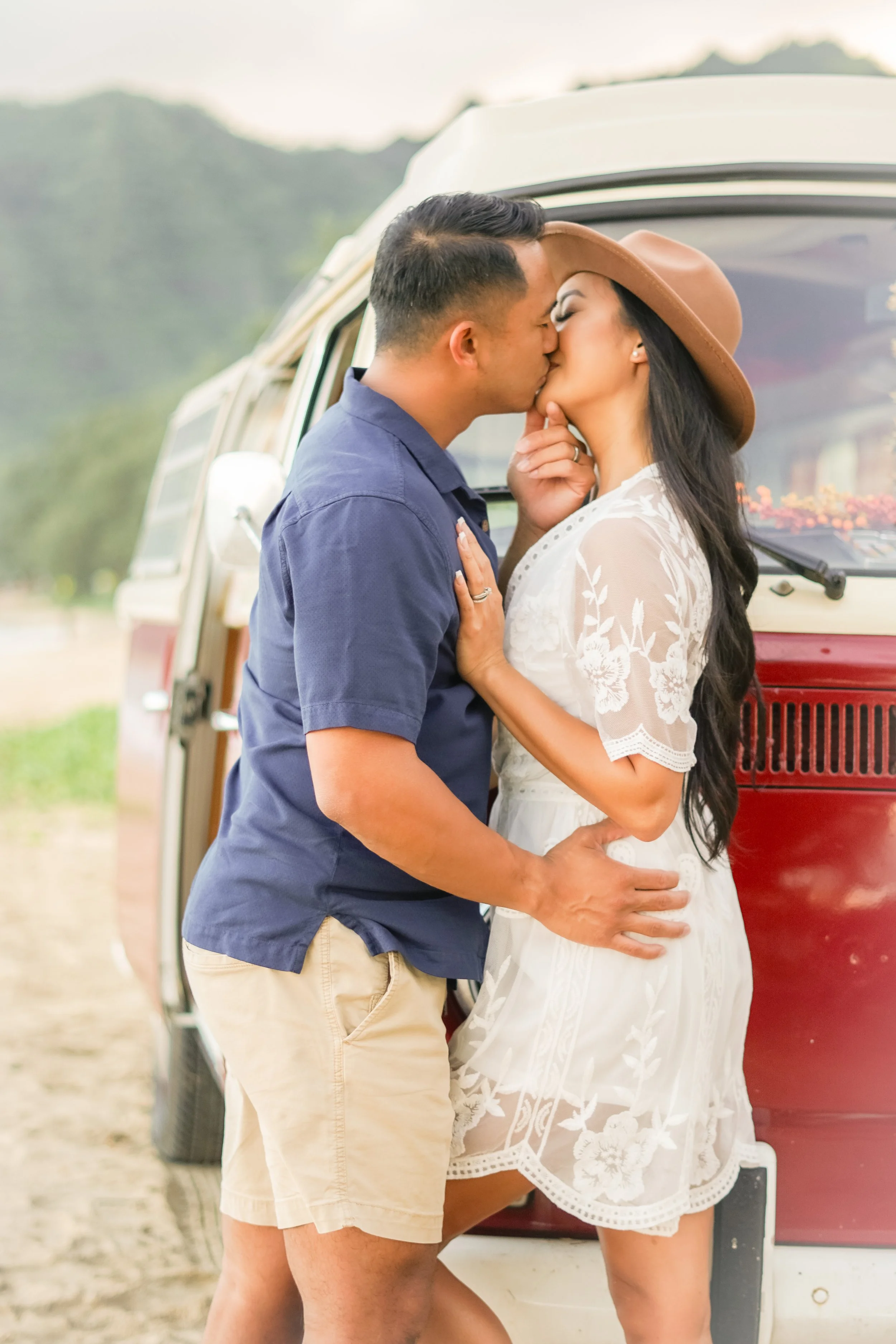 A couple kissing in front of a vintage van, with a scenic mountain background. photoshoot of a couple in oahu.