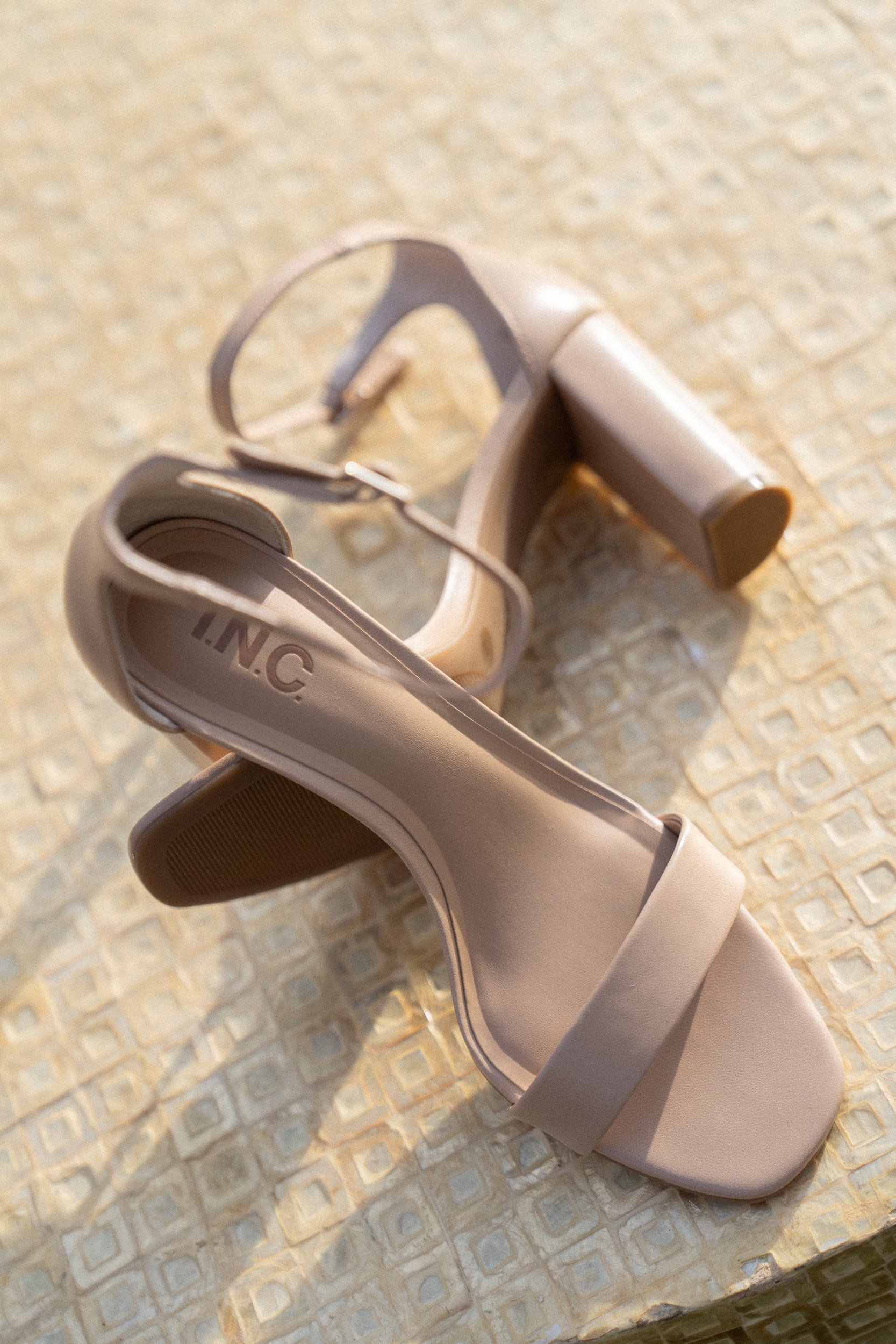 Beige high-heeled sandal with an ankle strap and a chunky heel placed on a textured surface.