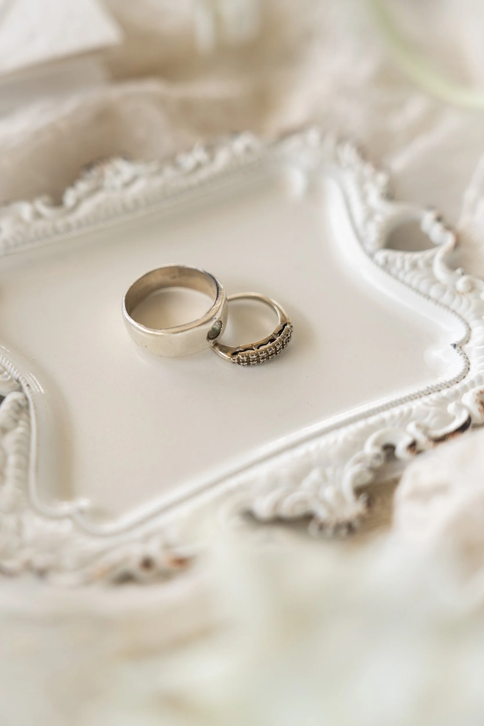 Close-up of two silver rings placed on a decorative white tray with ornate edges.