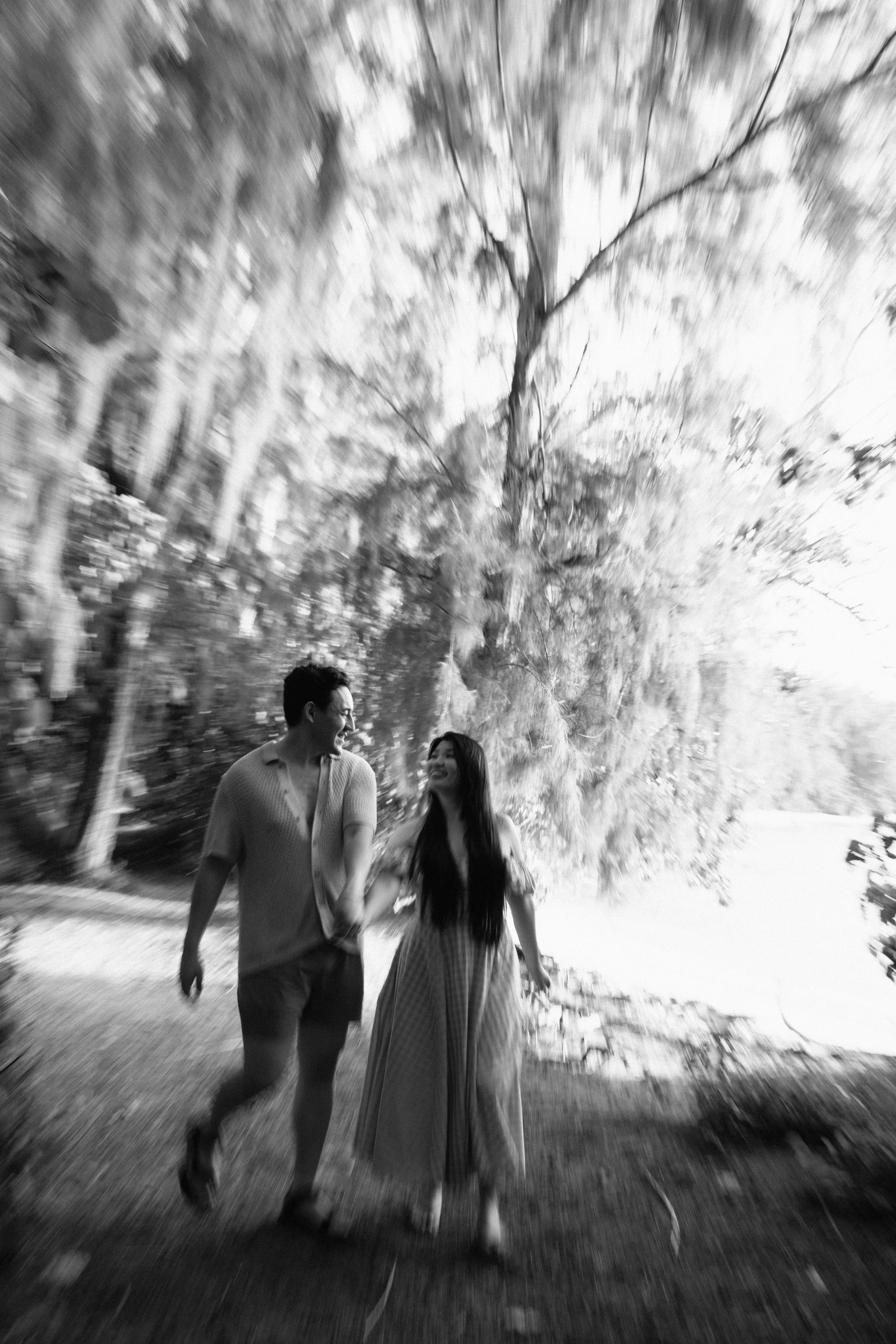 A black-and-white photo of a man and woman walking together outdoors with trees in the background.