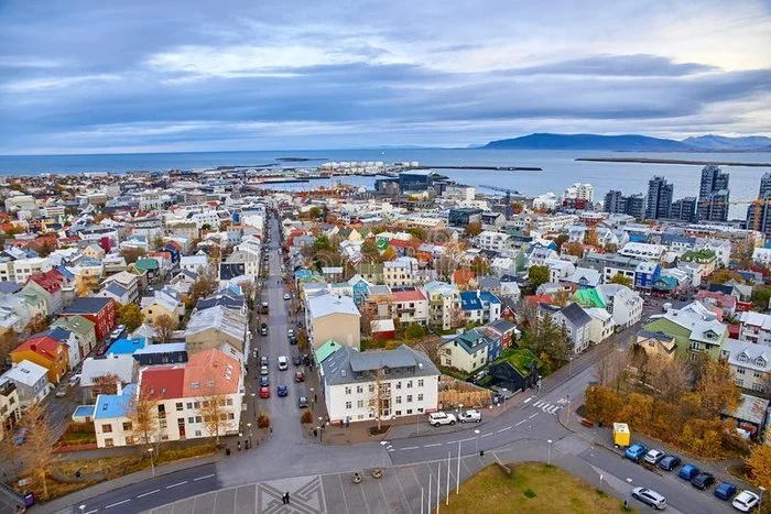 Aerial view of a colorful coastal city with residential buildings, a main street, and a body of water with mountains in the background.