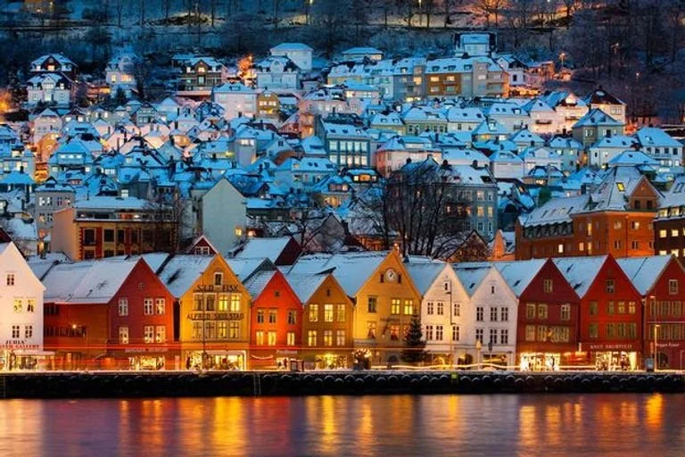 Colorful houses with snow on rooftops along a waterfront at dusk.