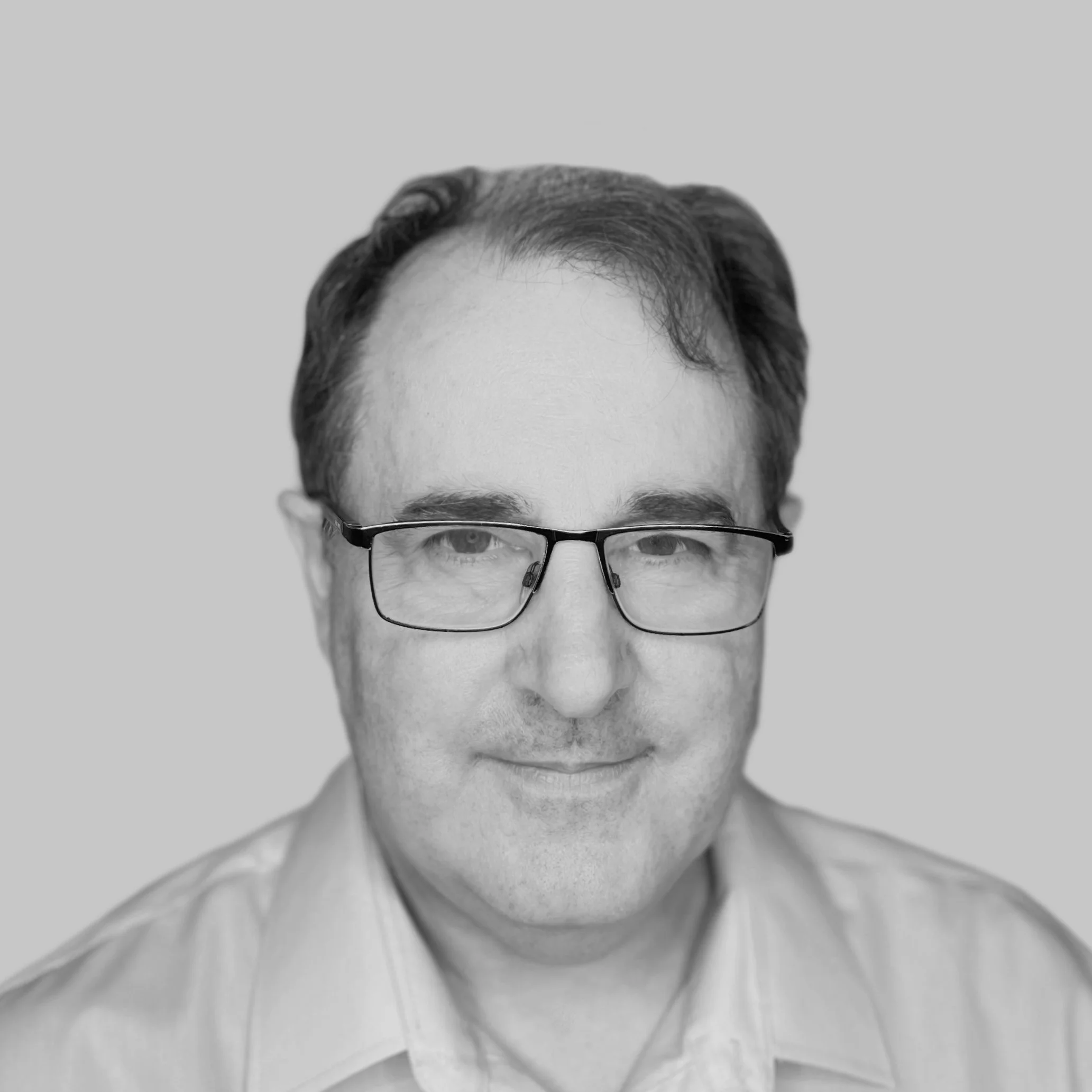 Black and white portrait of a man with glasses, short dark hair, wearing a light-colored shirt, smiling slightly, against a plain background.