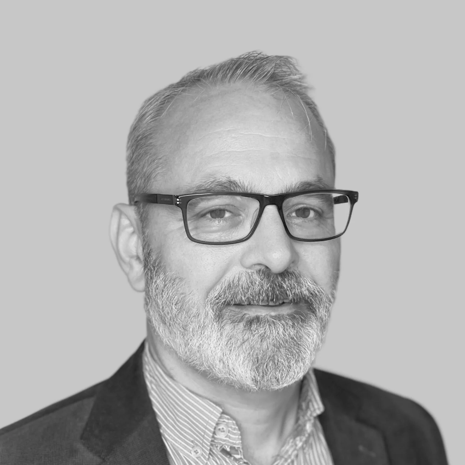 Black and white portrait of a middle-aged man with glasses, short hair, beard, wearing a suit jacket and collared shirt, against a plain background.
