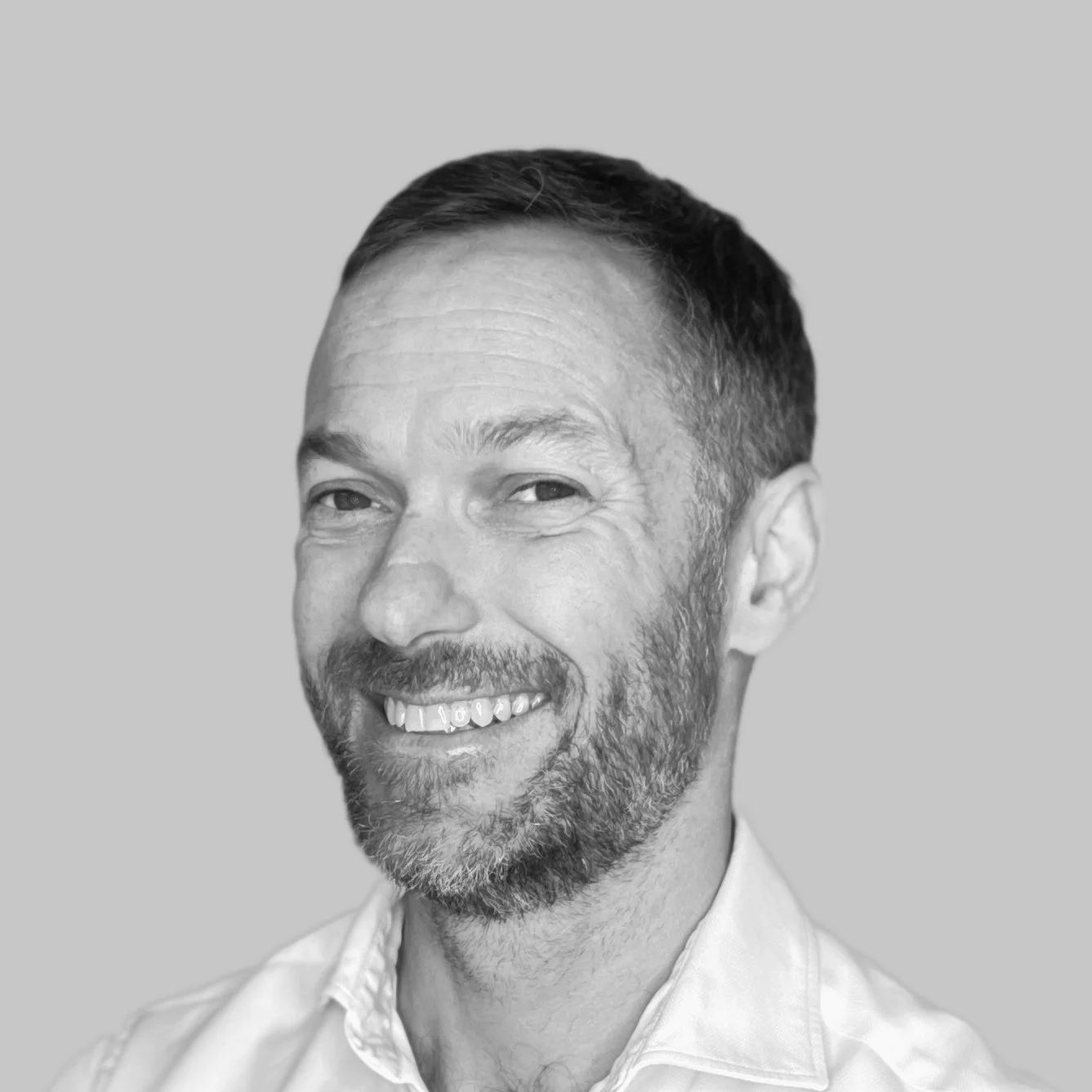 Black and white portrait of a smiling man with short hair, a beard, and a collared shirt, against a plain background.
