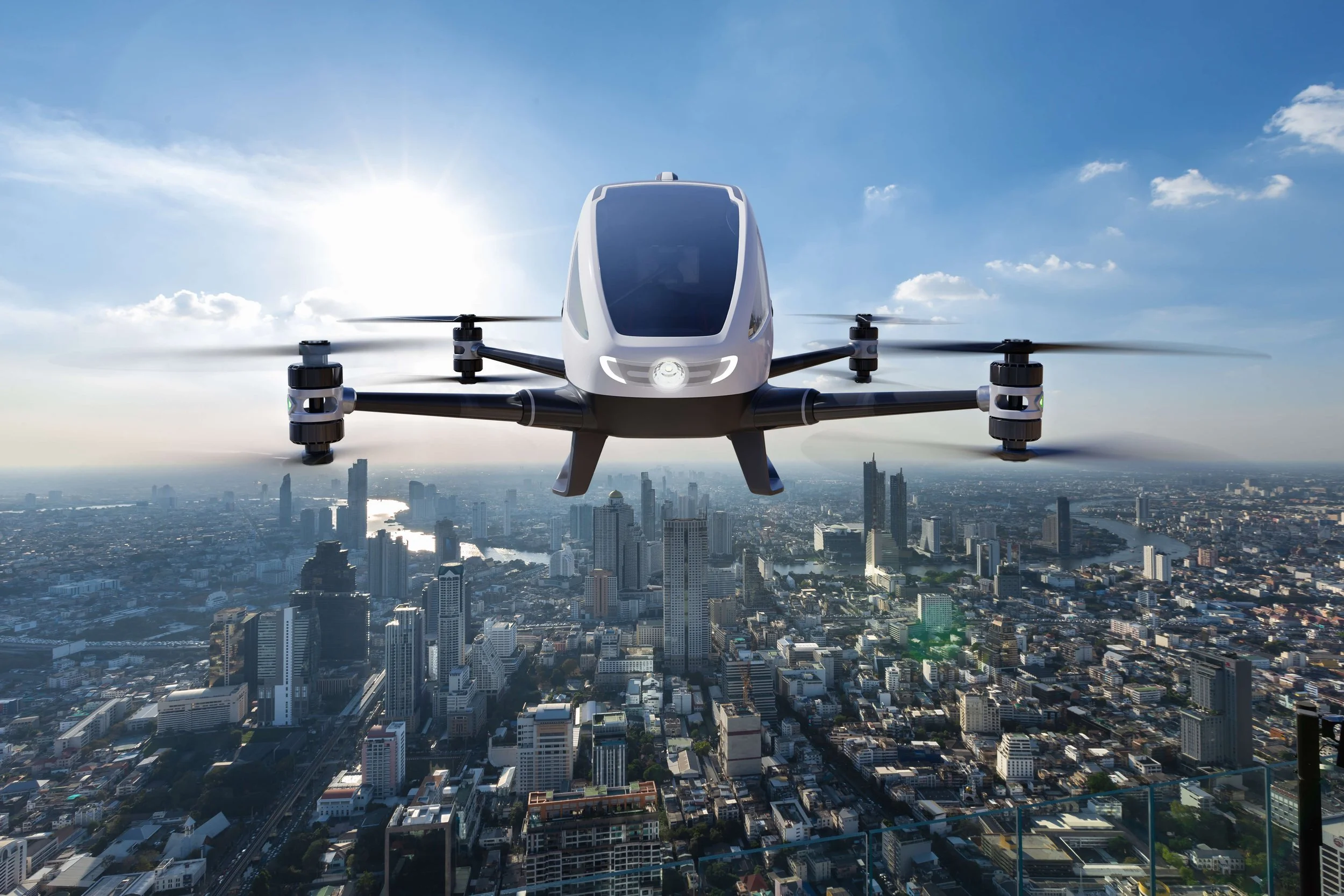 A futuristic electric drone flying over a city skyline during the daytime.