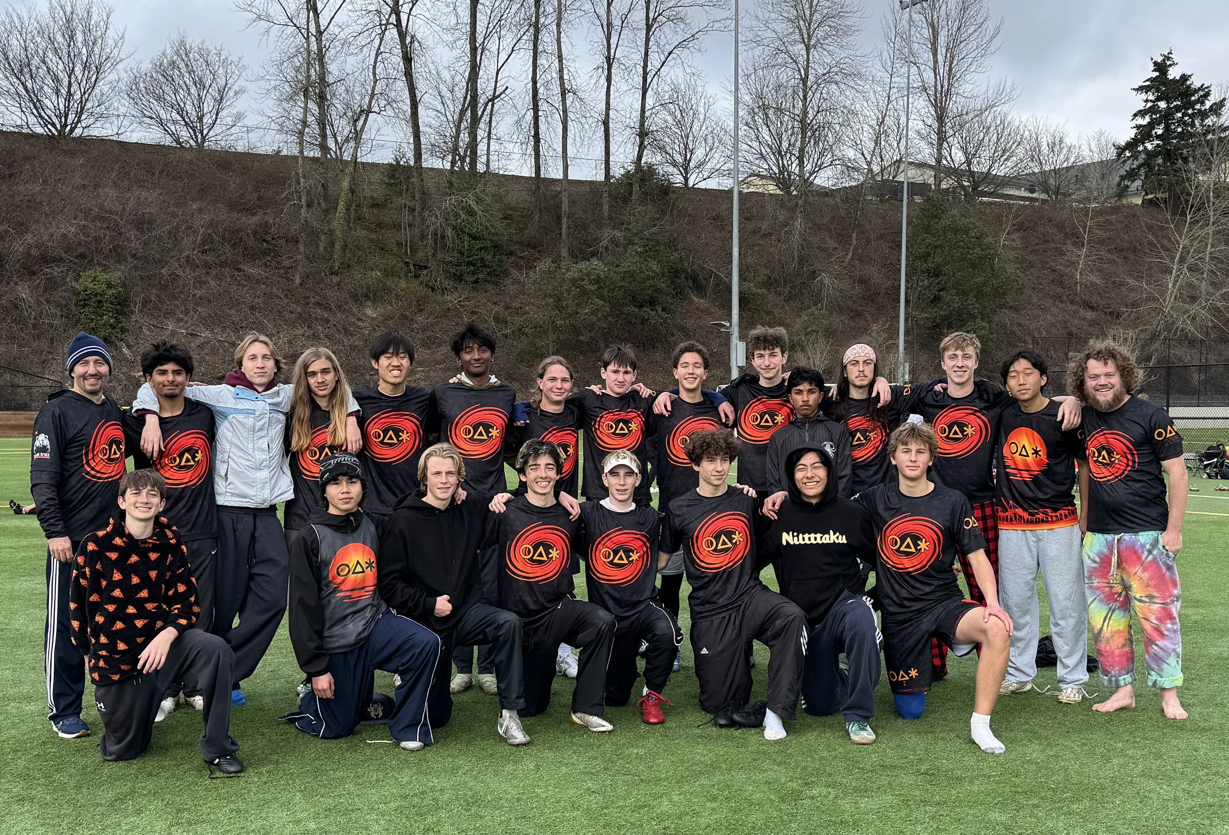 Group of young people in black jerseys with red and orange logos, standing and kneeling on a sports field, team photo