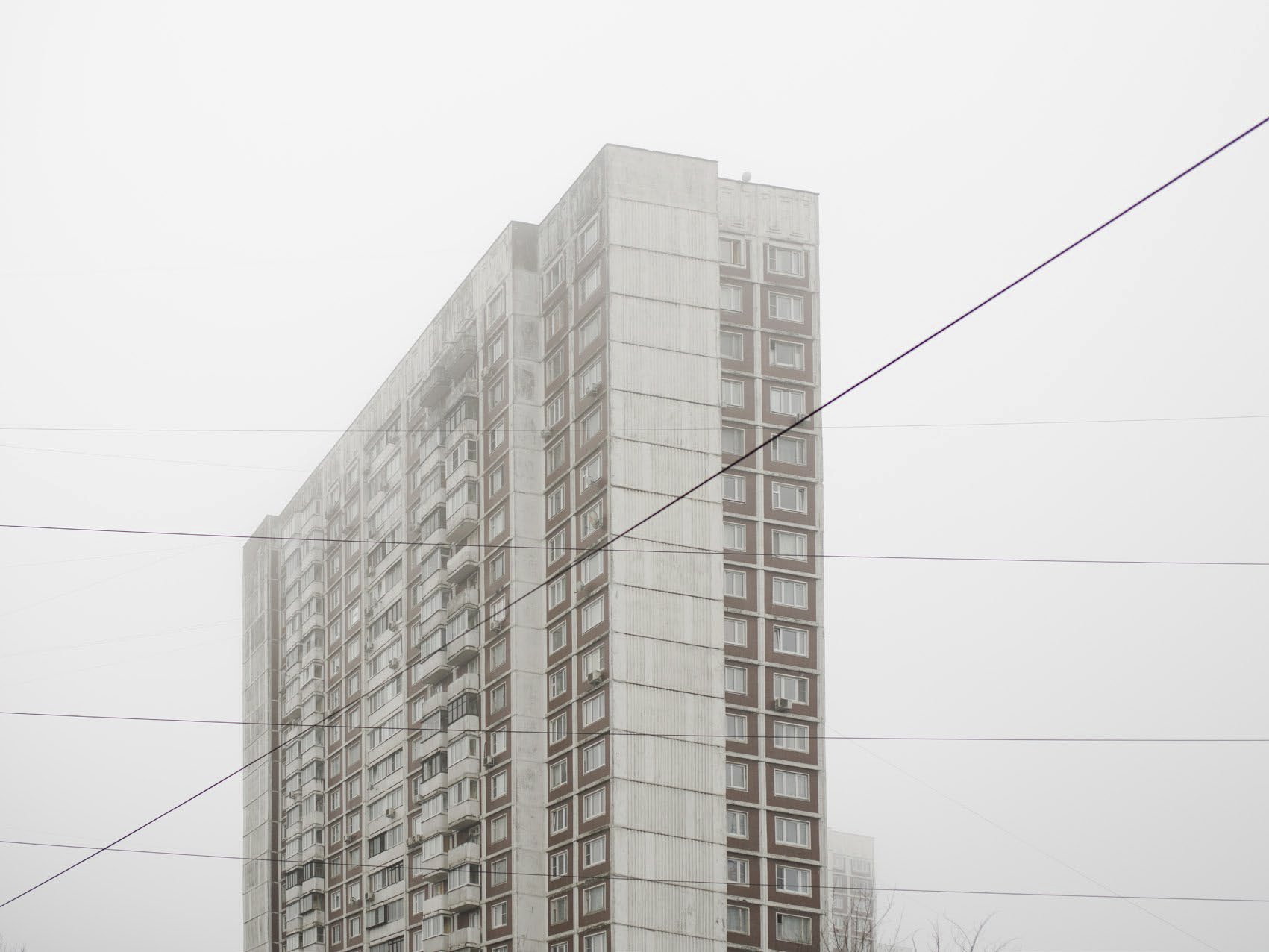 A tall apartment building on a foggy day, with multiple floors and windows, and power lines crossing in the foreground.