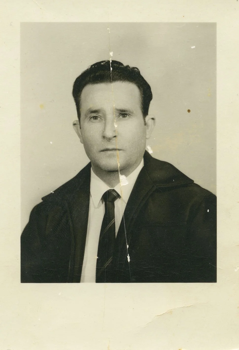 Black and white portrait photograph of a man wearing a suit and tie, with a serious expression, visible damage, and a vertical crease in the middle.